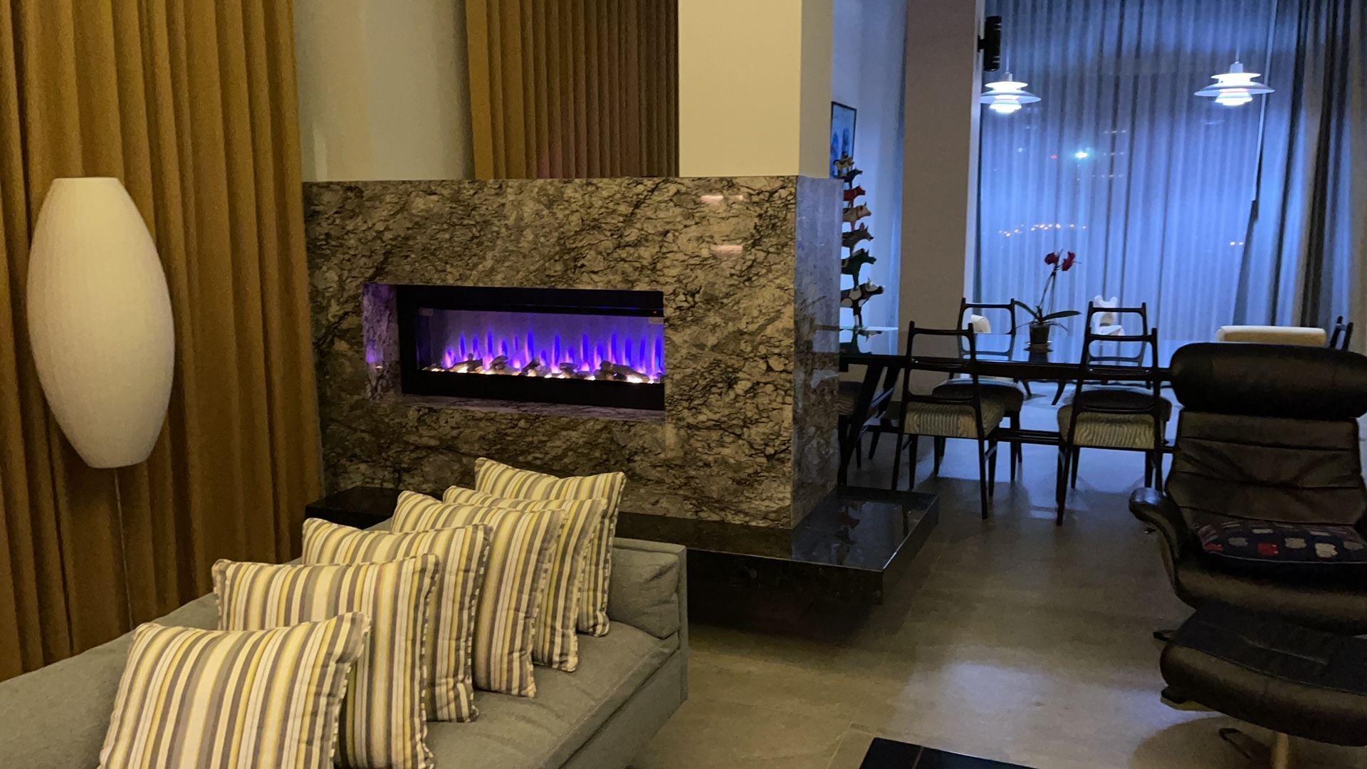 Modern living room with stone fireplace, striped chair, and dining area in the background