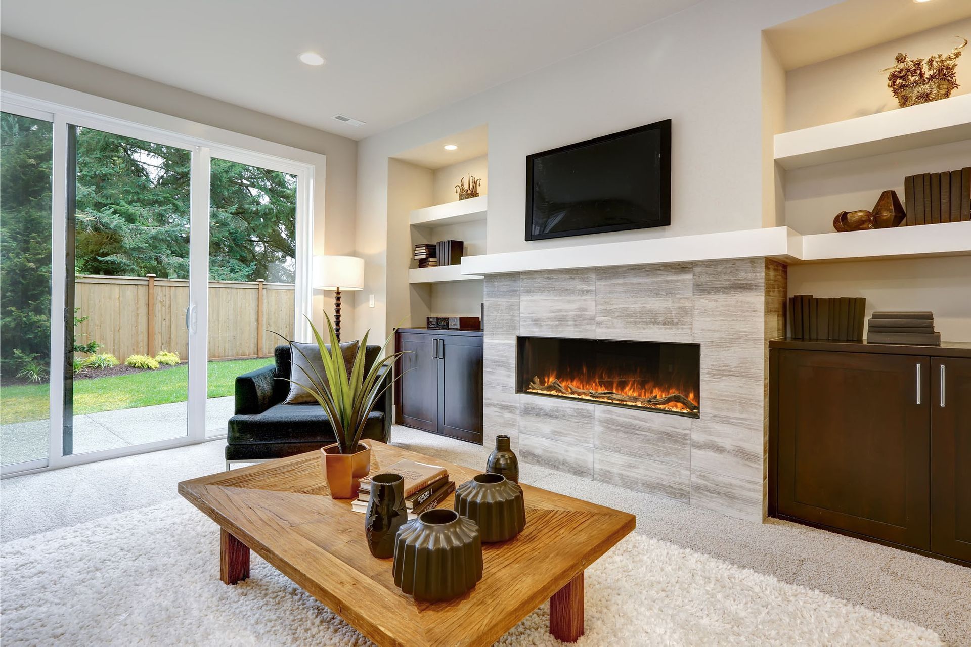 Modern living room with a fireplace, wall-mounted TV, sliding glass doors, and a wooden coffee table