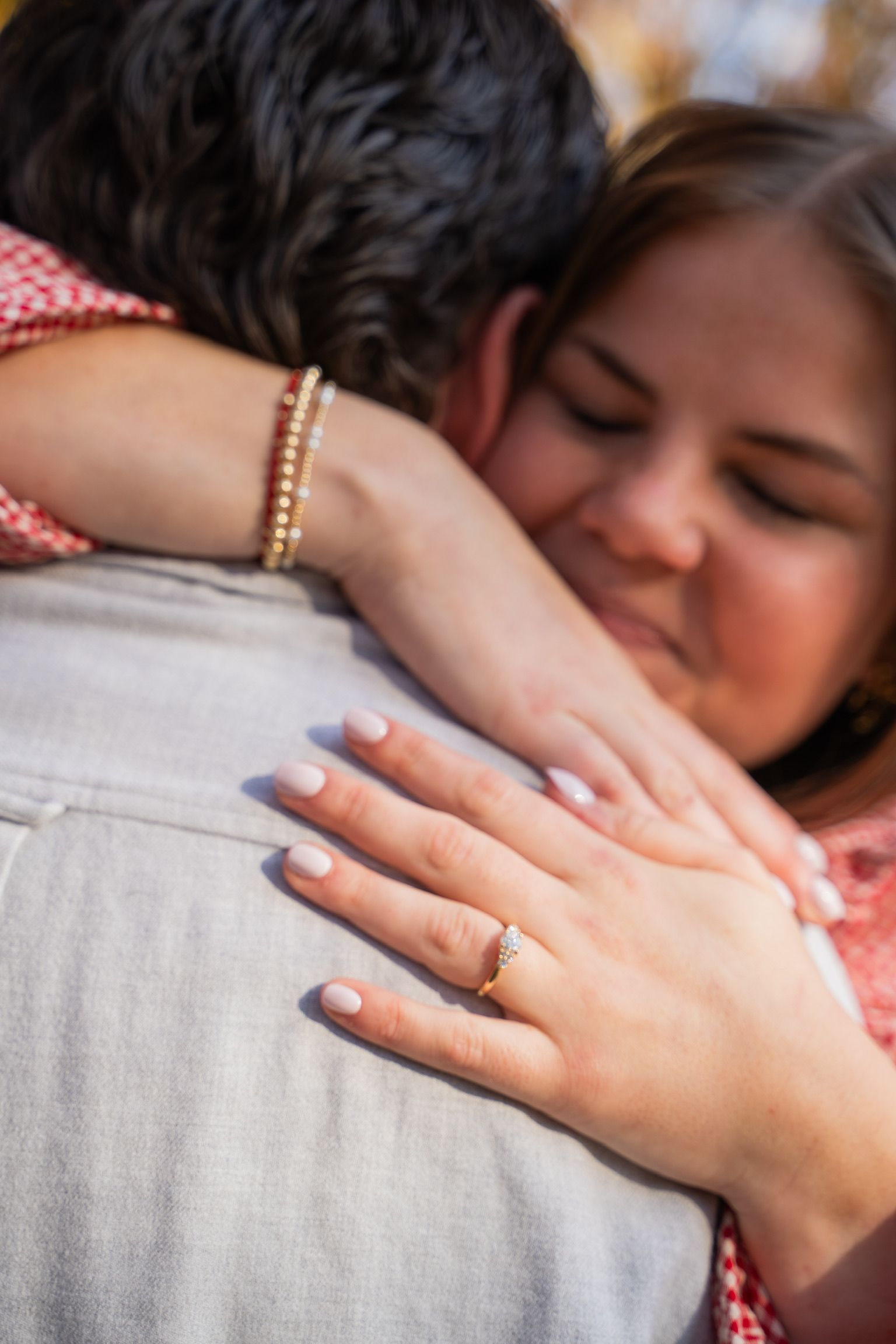 Two people embracing closely, one hand with a gold ring resting on a gray shirt.