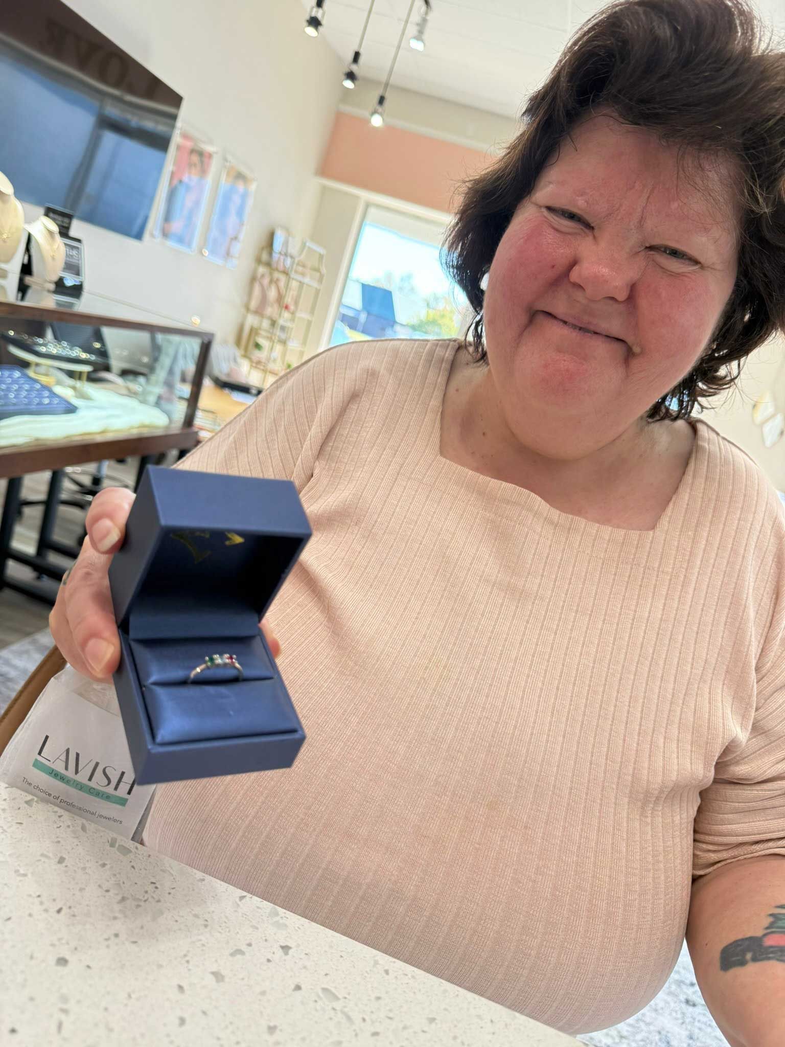 Woman smiling while holding an open blue ring box in a jewelry store.