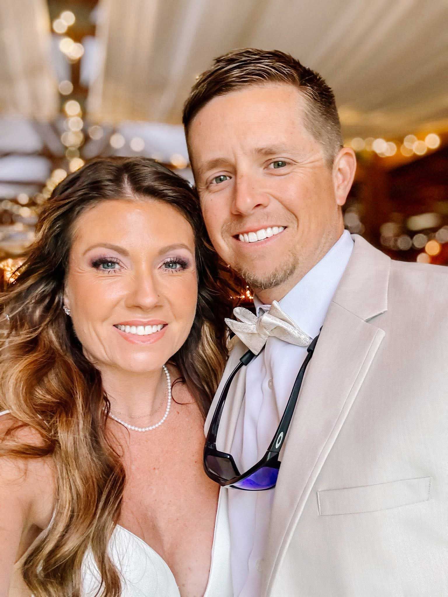 Smiling couple in formal attire posing at an elegant indoor event with warm lights.