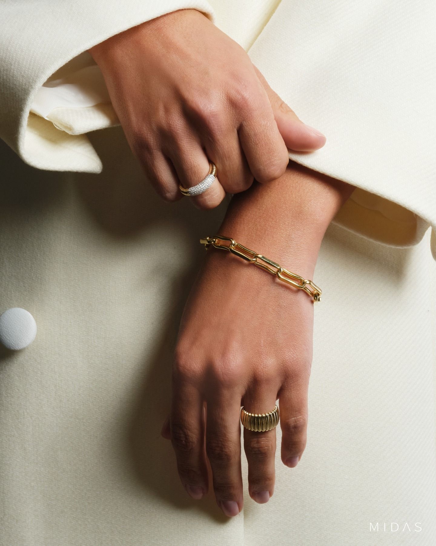 Hands with gold jewelry against a cream background
