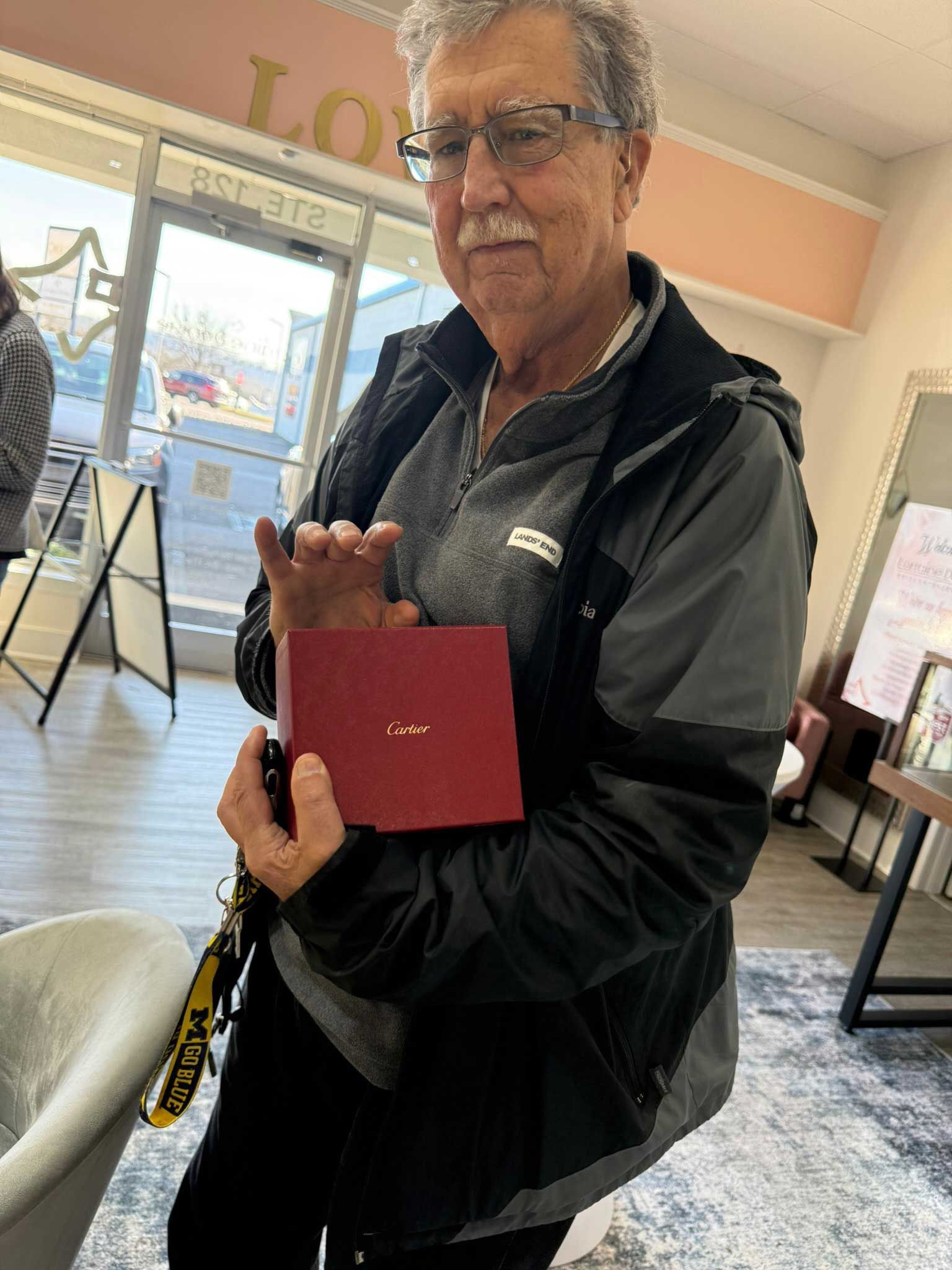 Man holding a red box in a bright indoor room with chairs and a rug