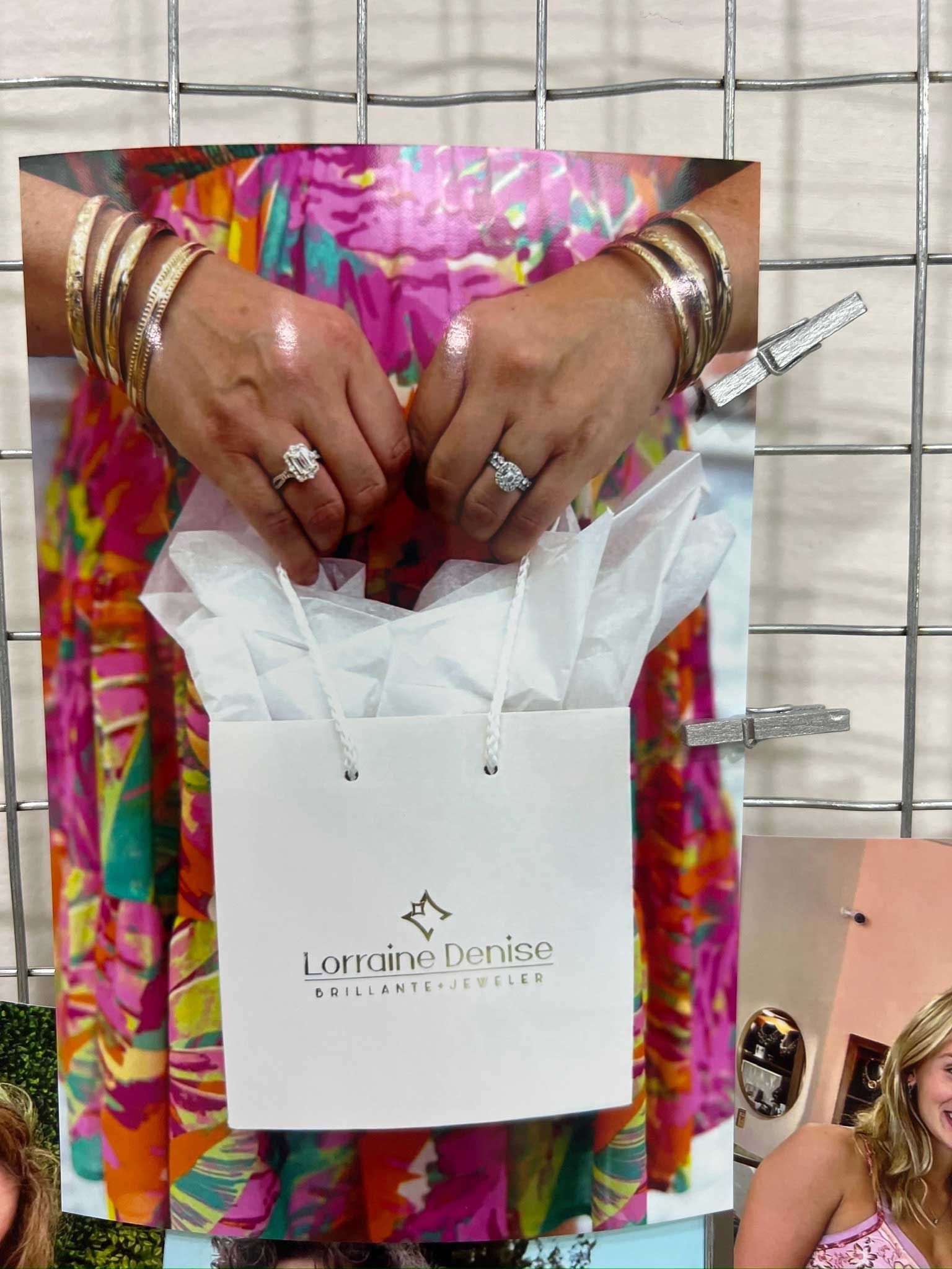 Hands holding a white gift bag with tissue paper, wearing colorful clothing and gold bracelets.