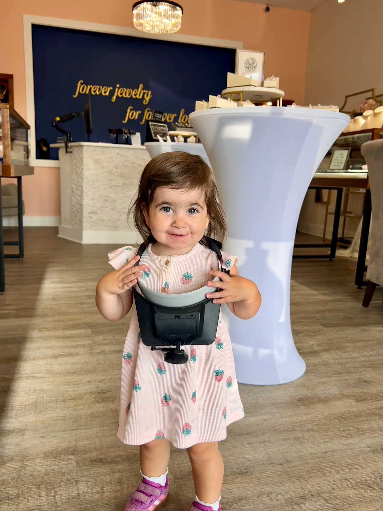 Young child holding a small black bag in a decorated banquet hall beside a tall white table
