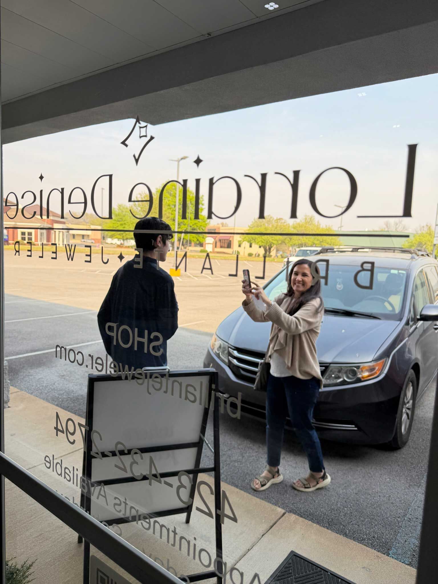 Woman posing beside a black car outside a glass storefront with reversed lettering.