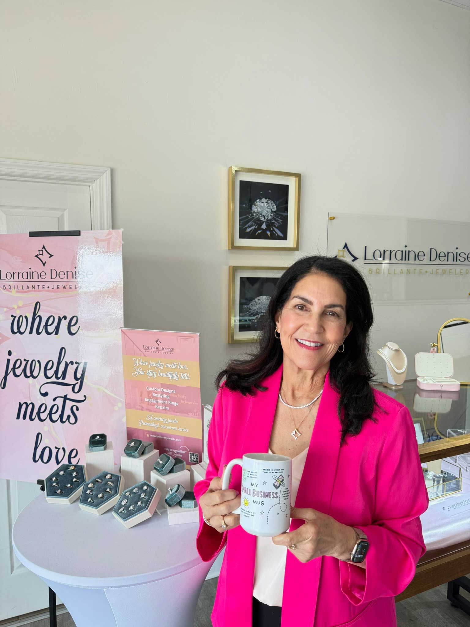 Woman in pink jacket holding a mug beside a display with jewelry boxes and signage