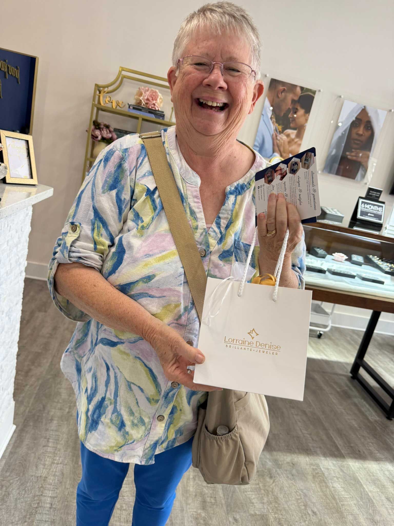 Smiling person holding a white gift bag in a bright shop with framed artwork and displays nearby