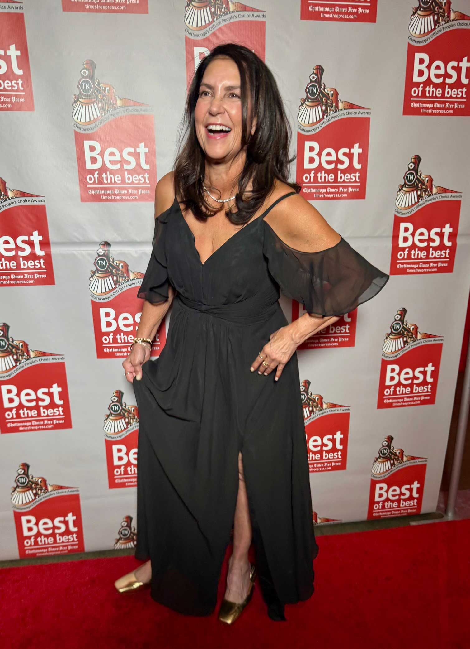 Woman in a black off-shoulder dress posing on a red carpet before a Best awards backdrop