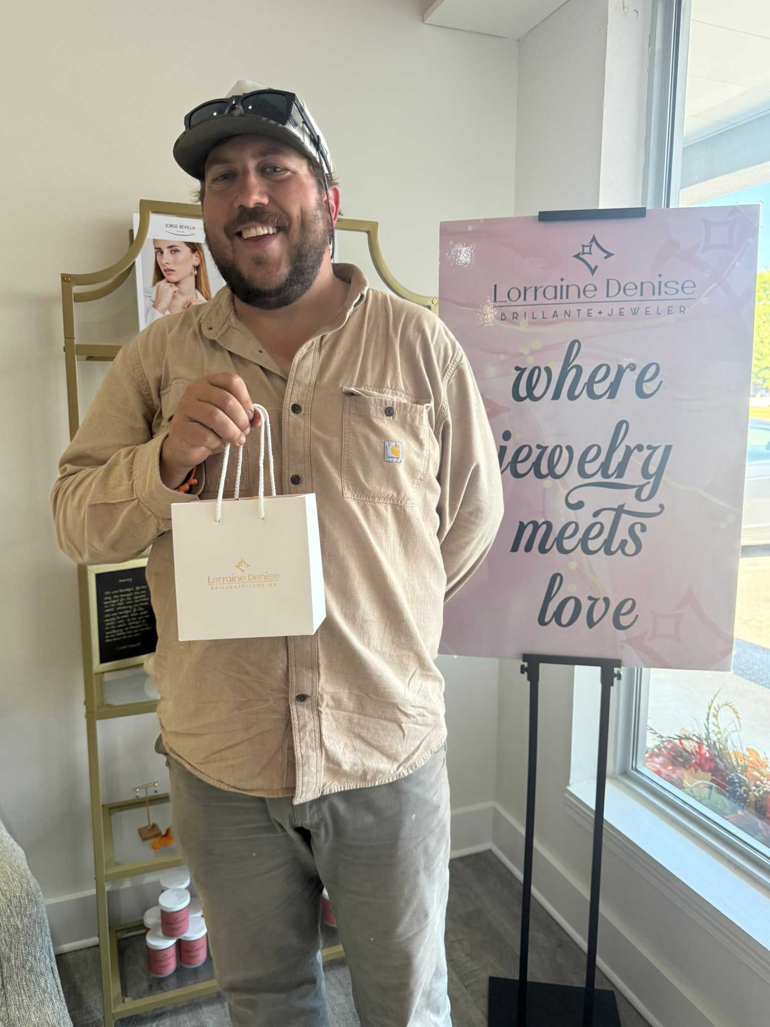 Man holding a white gift bag beside a sign in a bright shop window