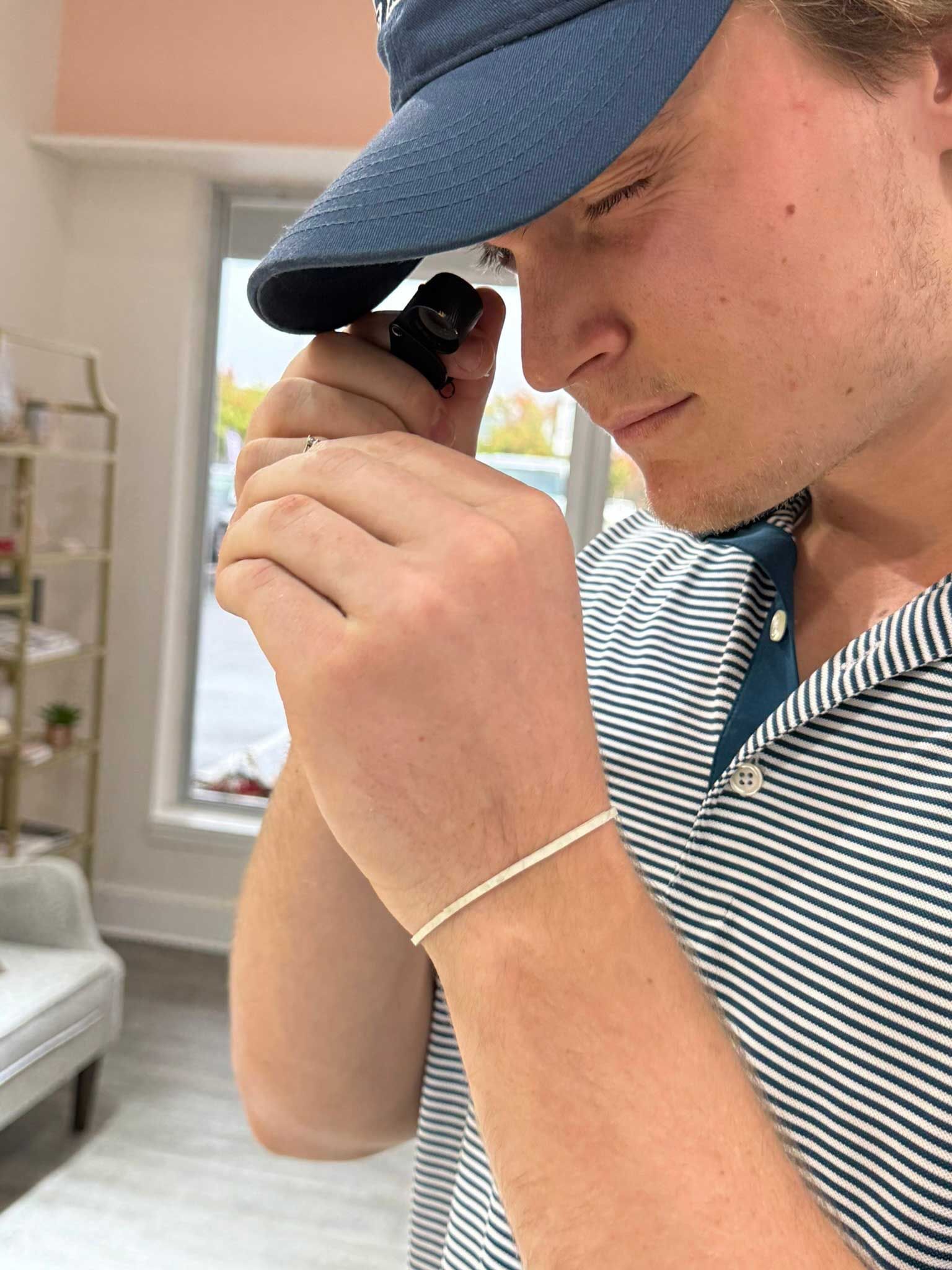 Person in a blue cap closely examining a small object indoors near a window.