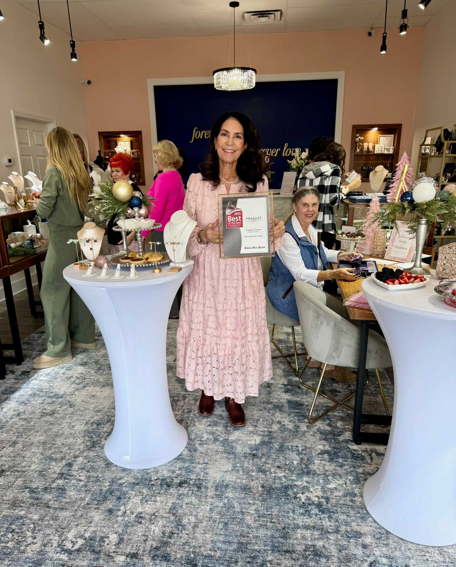 Woman in a pink dress holding a framed sign at a decorated indoor event booth.