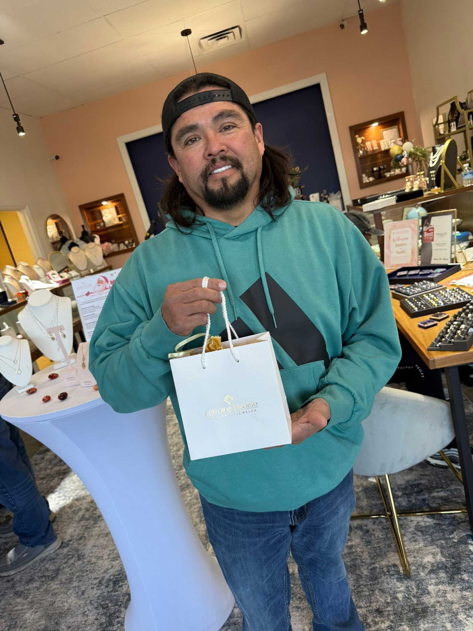 Person in a teal hoodie holding a white gift bag at an indoor party or event.