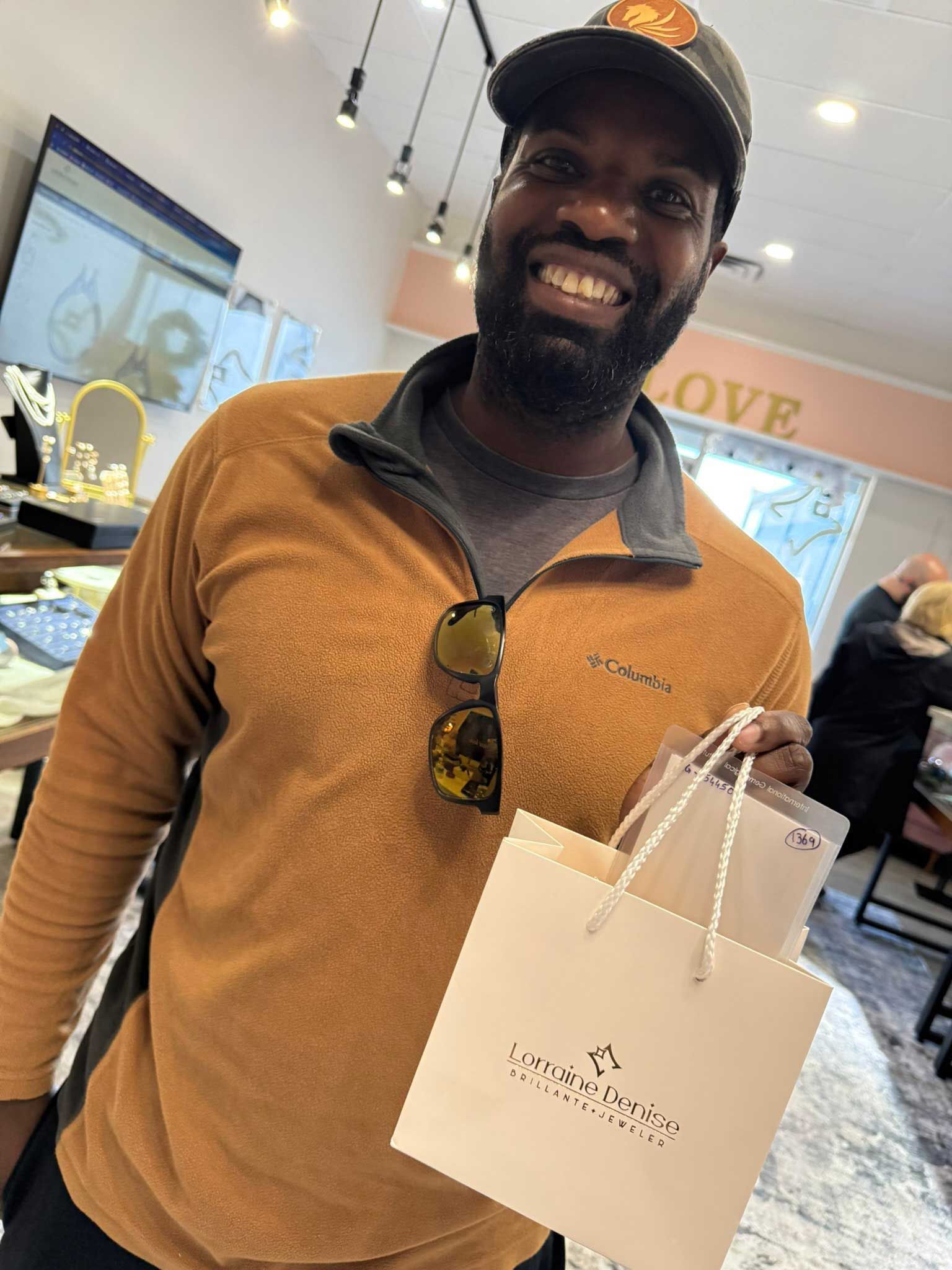 Smiling man in an orange shirt and cap holding a white shopping bag in a bright store