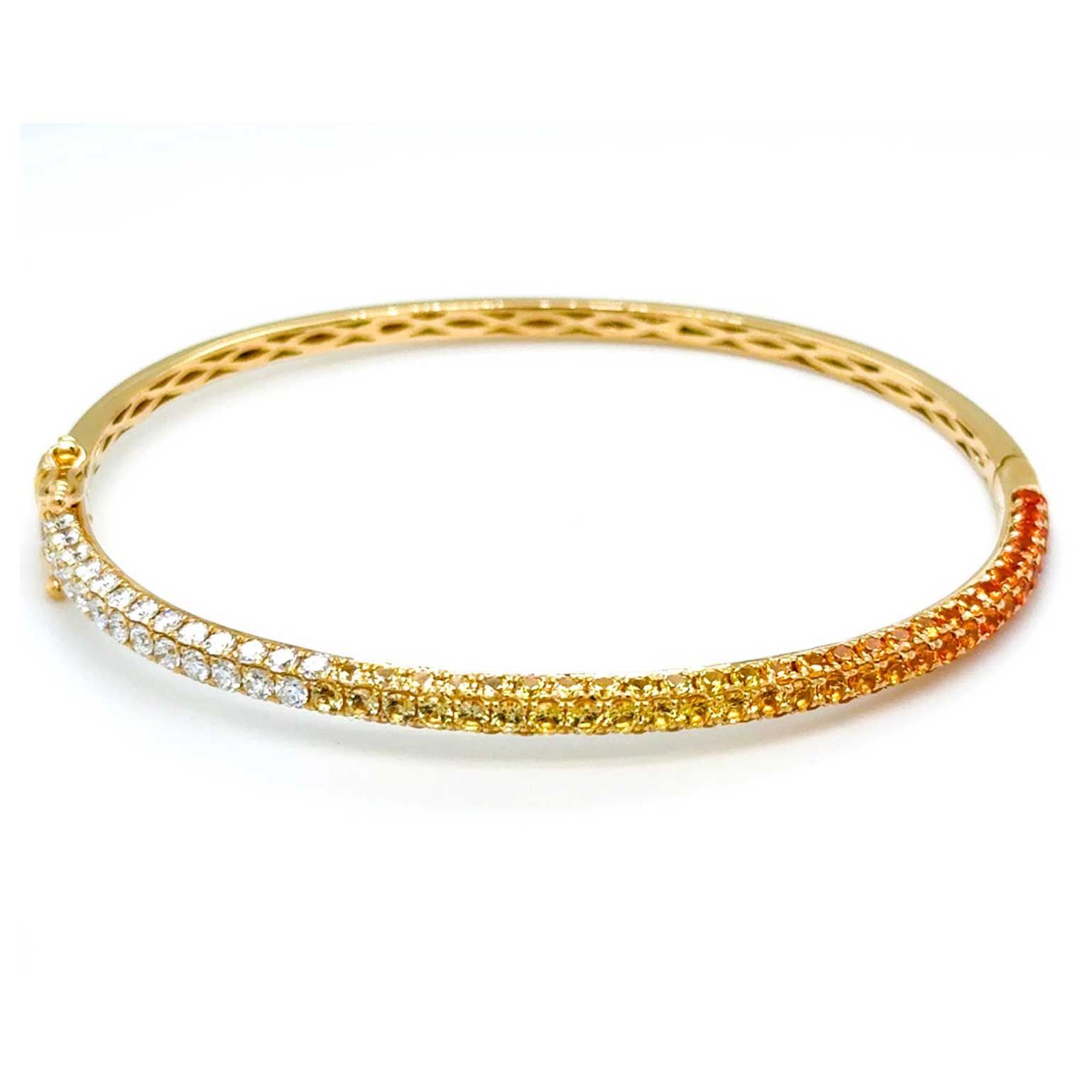 Gold bangle bracelet with white and orange gemstones on a white background