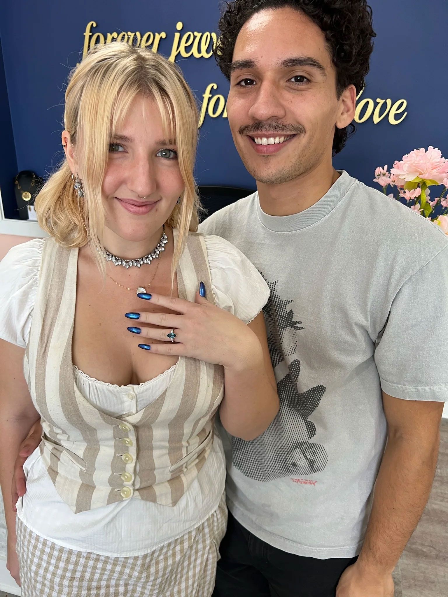 Couple smiling, woman showing off engagement ring at jewelry store.