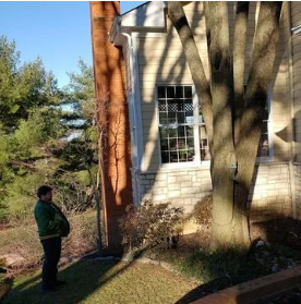A man in a green jacket is standing in front of a house.