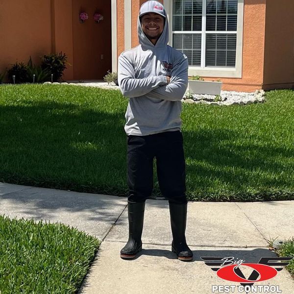 A man wearing a hoodie and boots stands on a sidewalk in front of a house