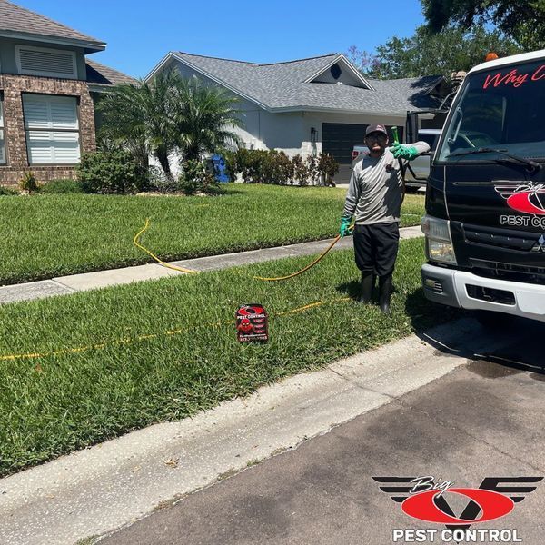 A man spraying a lawn next to a truck that says pest control