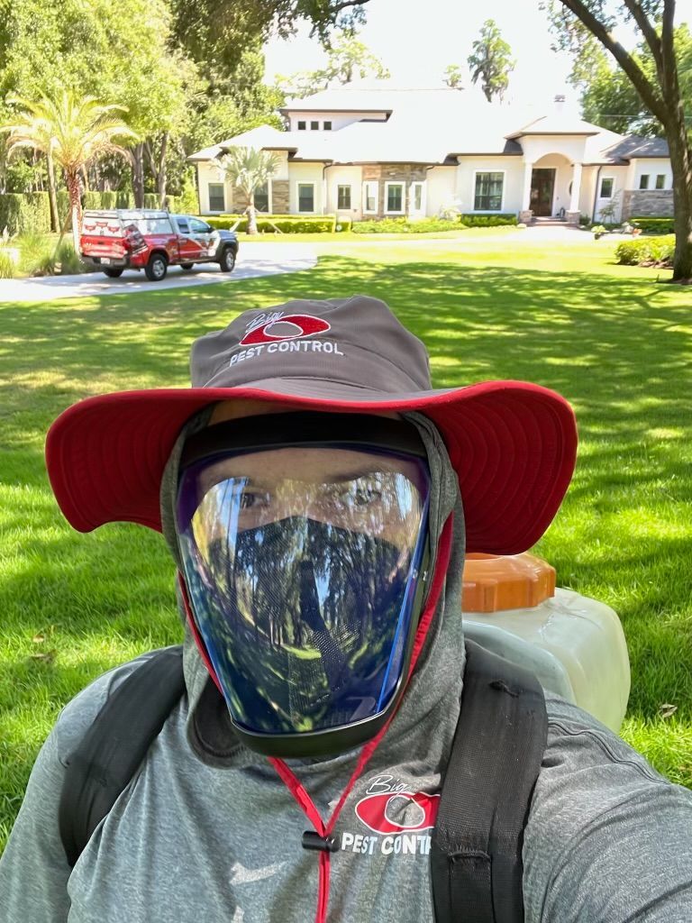 Man in safety gear spraying a lawn with a large house in the background.