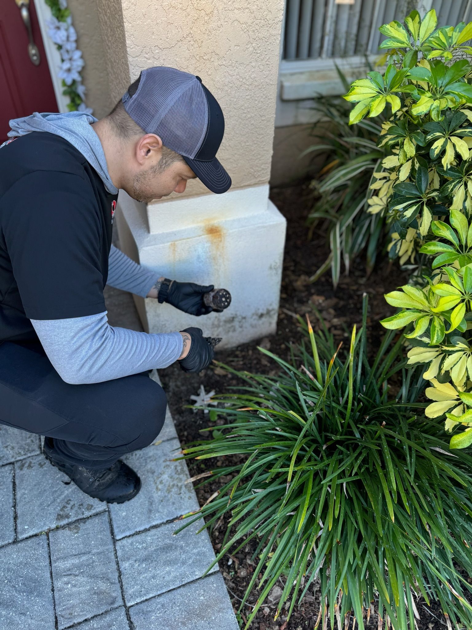 A man is kneeling down in front of a building holding a tool.