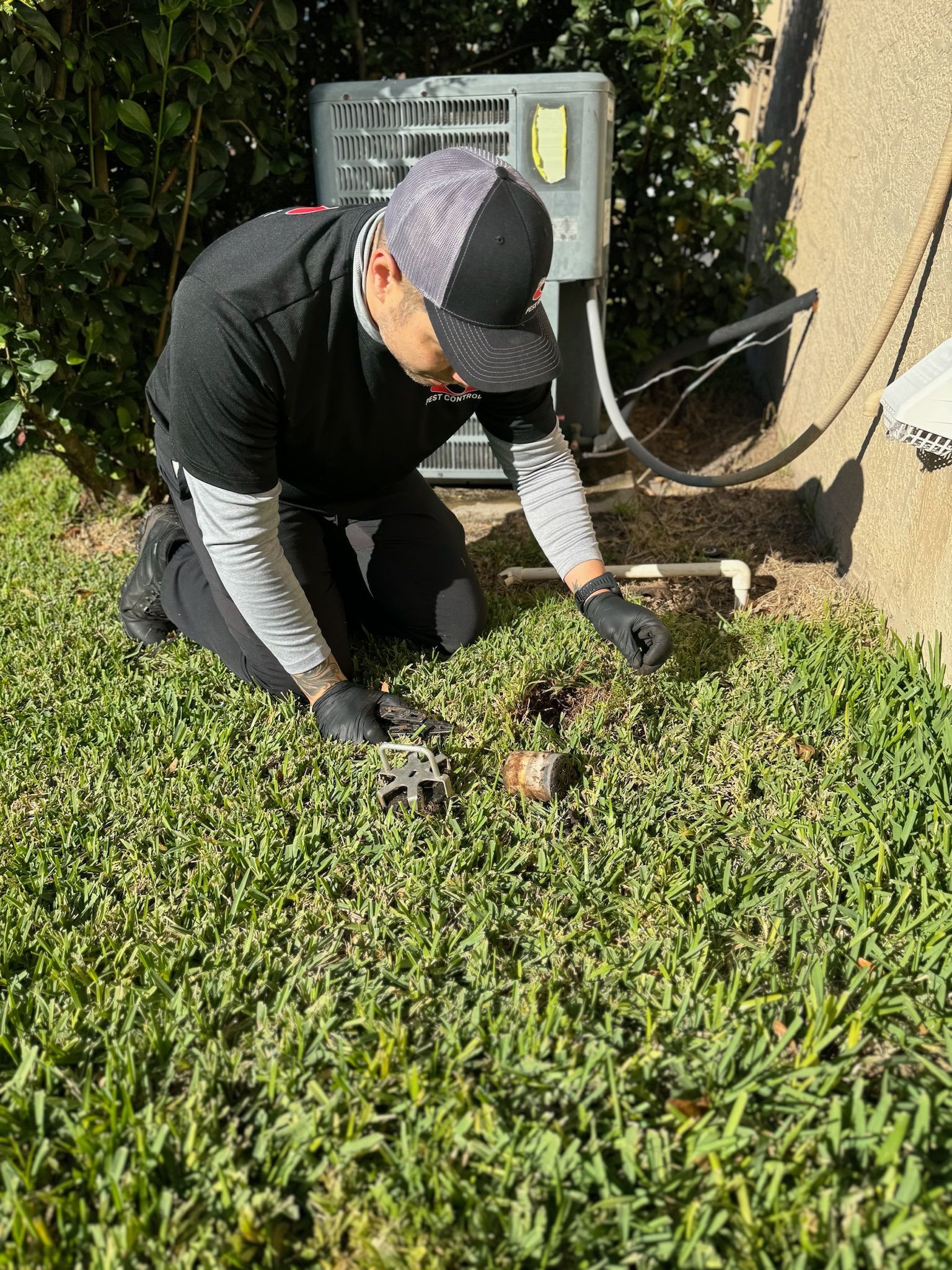 A man is kneeling down in the grass with a tool in his hand.