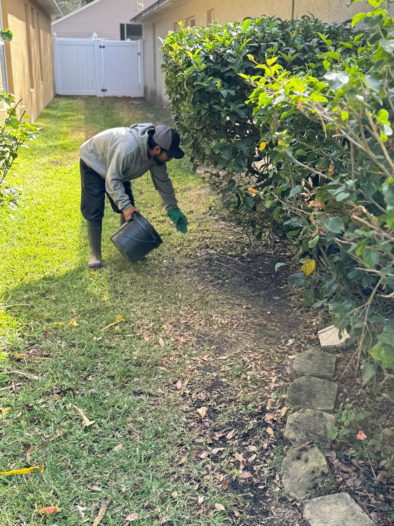 A man is kneeling down in the grass holding a bucket.