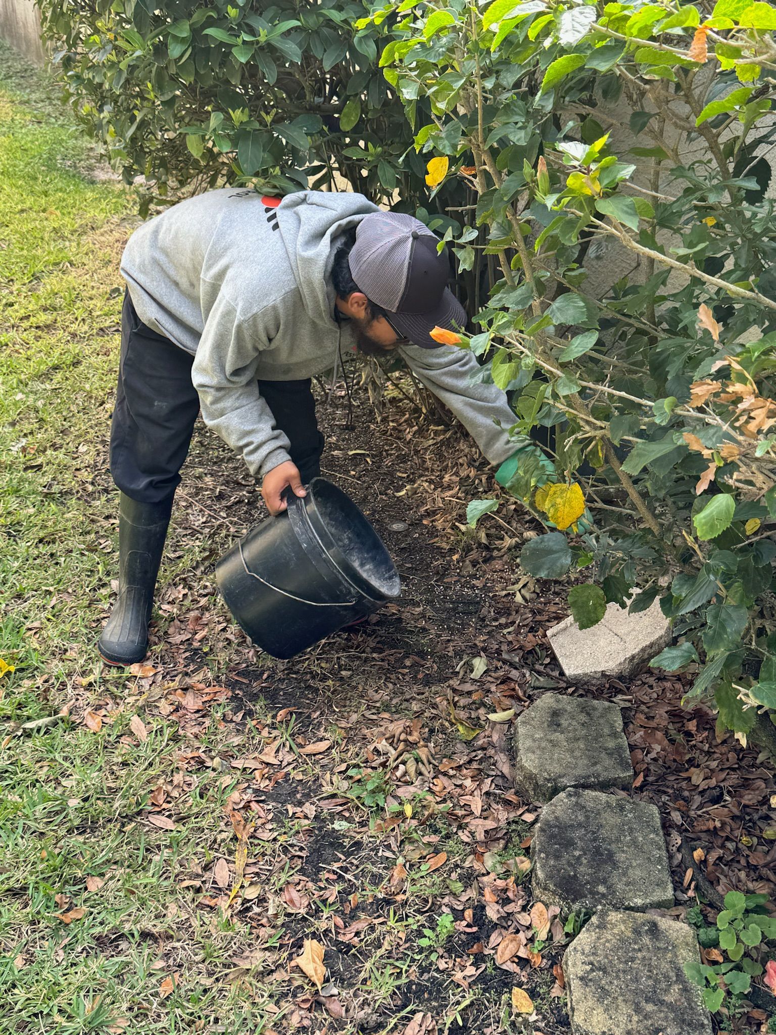 A man is kneeling down in a garden with a bucket and shovel.
