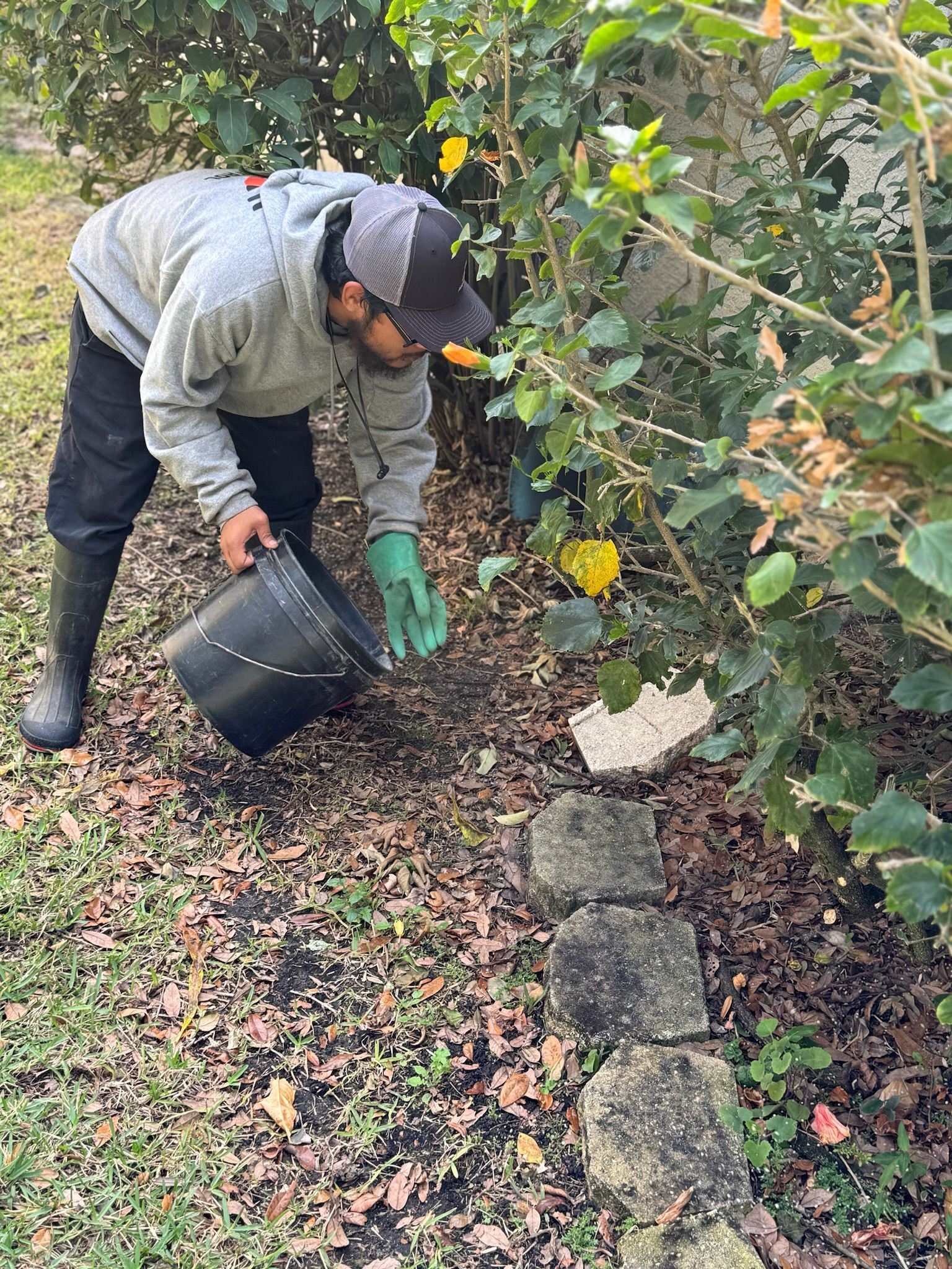 A man is kneeling down in the dirt holding a black bucket.