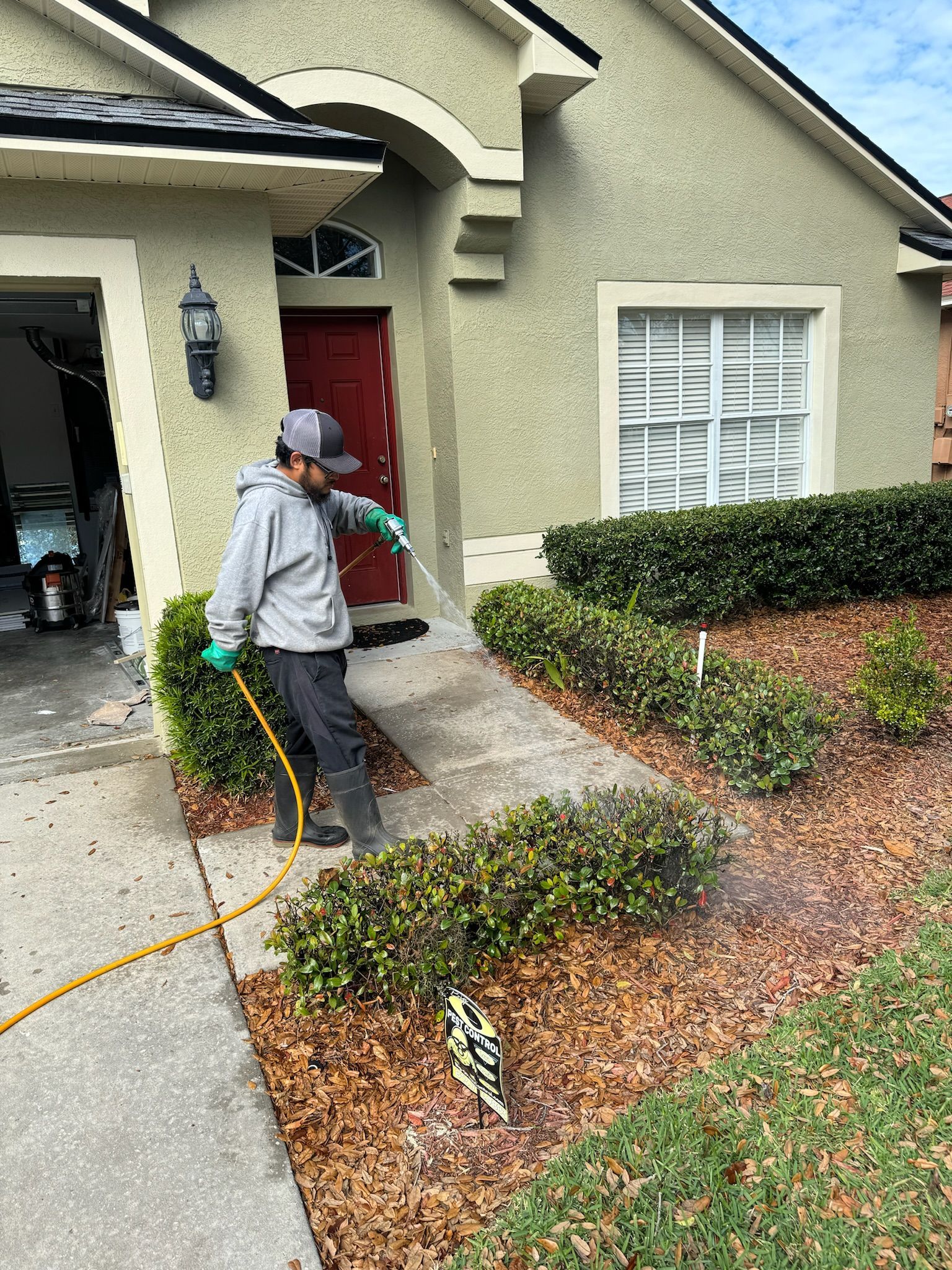 A man is spraying plants in front of a house with a hose.