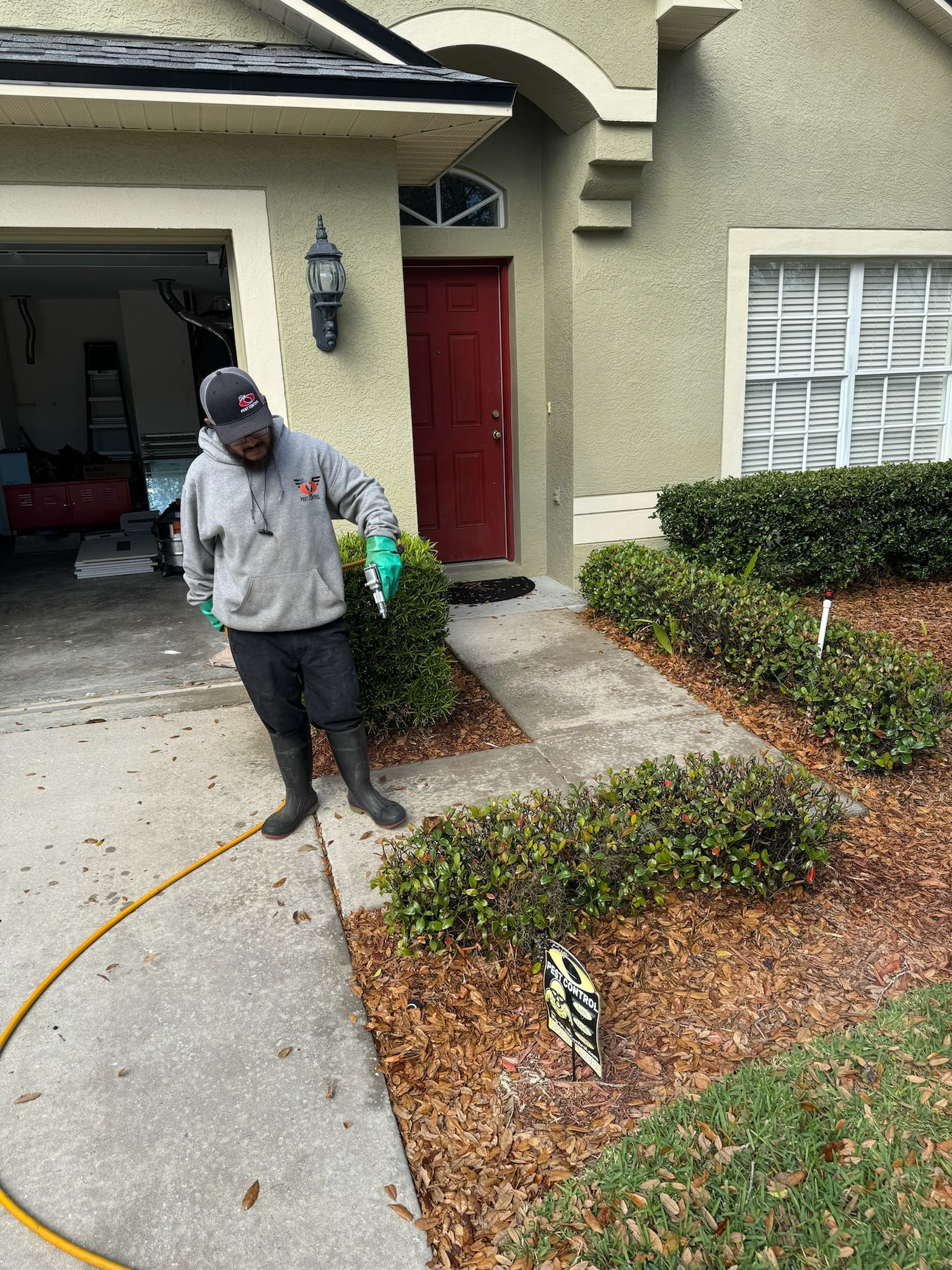 A man is spraying leaves on the sidewalk in front of a house.