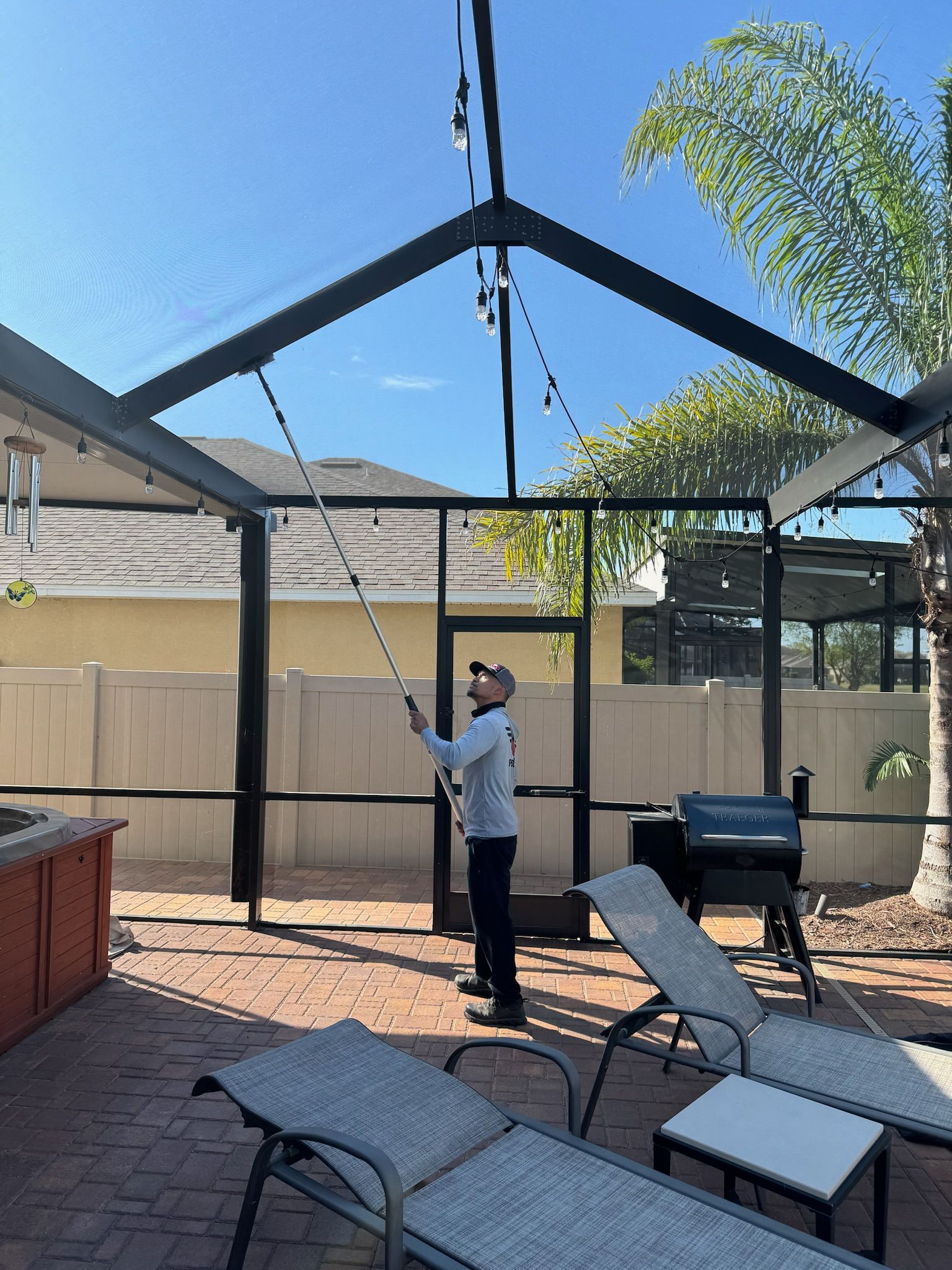 A man is cleaning a screened in porch with a hose.