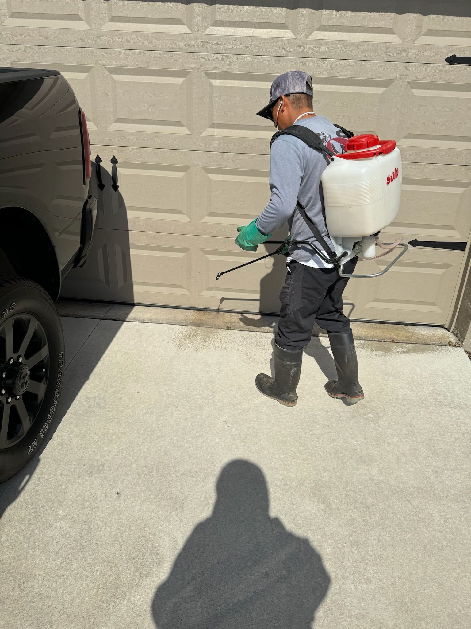 A man is spraying a garage door with a backpack sprayer.
