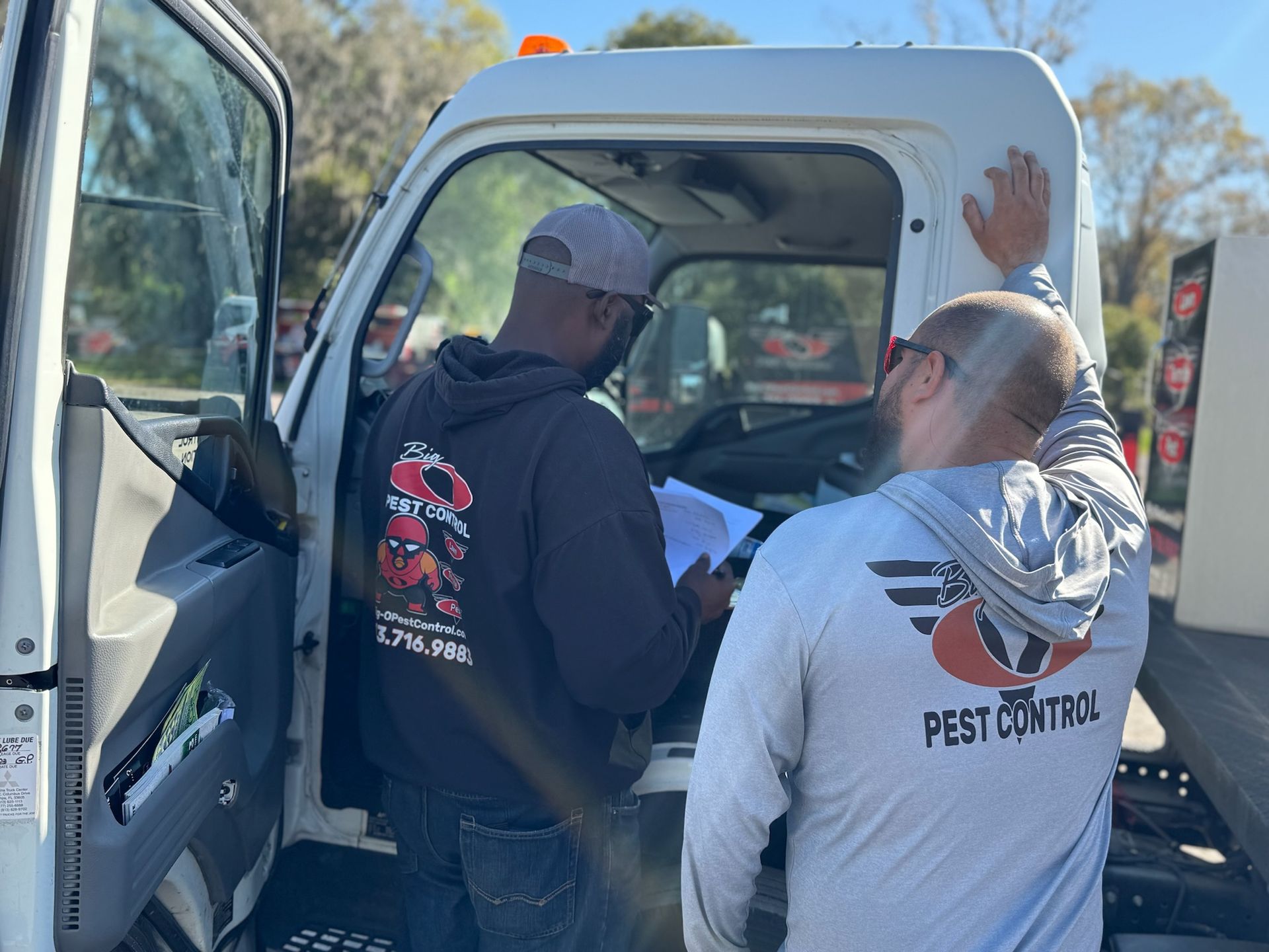 Two men are standing in the back of a truck looking at a piece of paper.