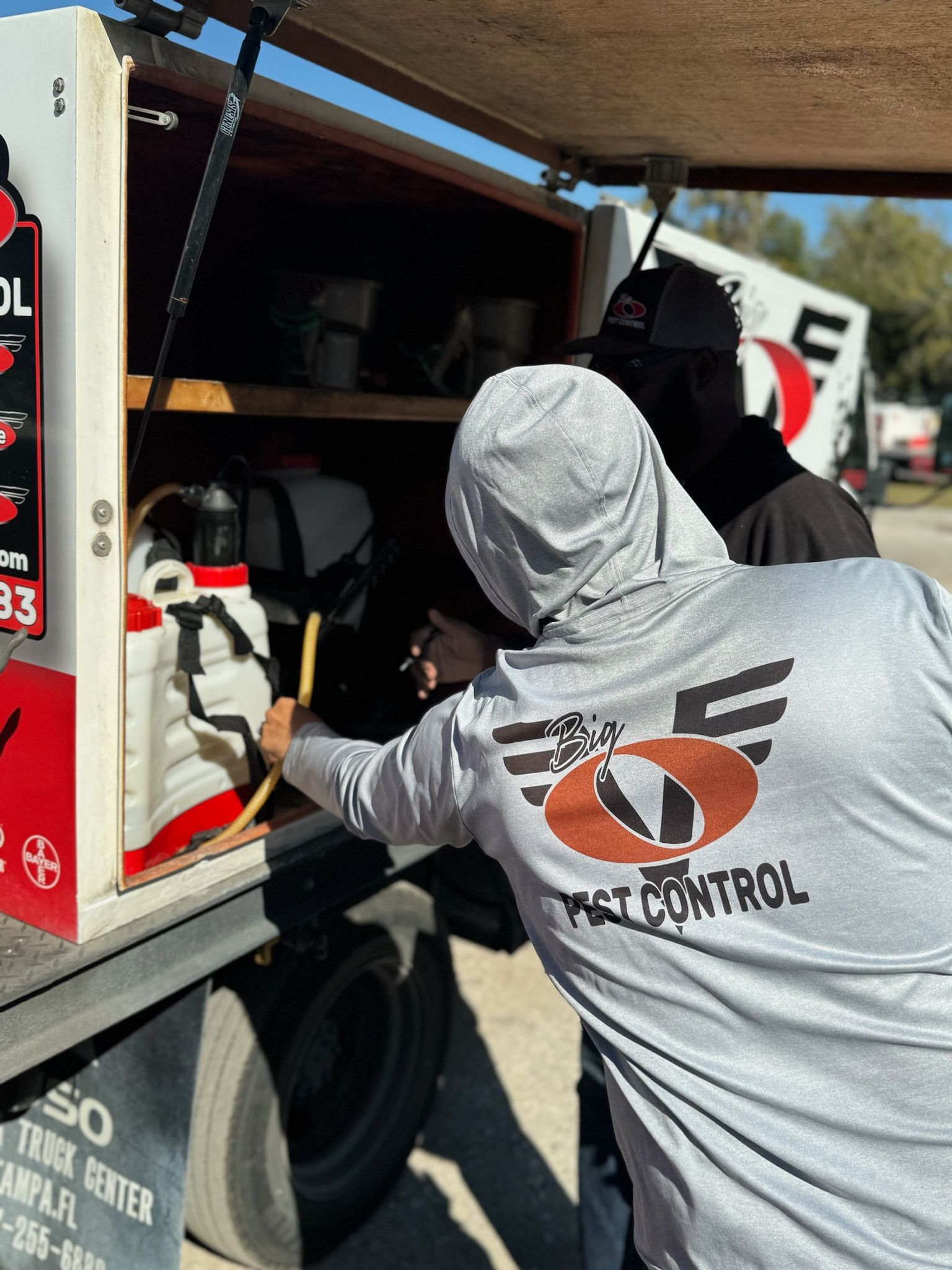 A man wearing a shirt that says pest control is working on a truck.