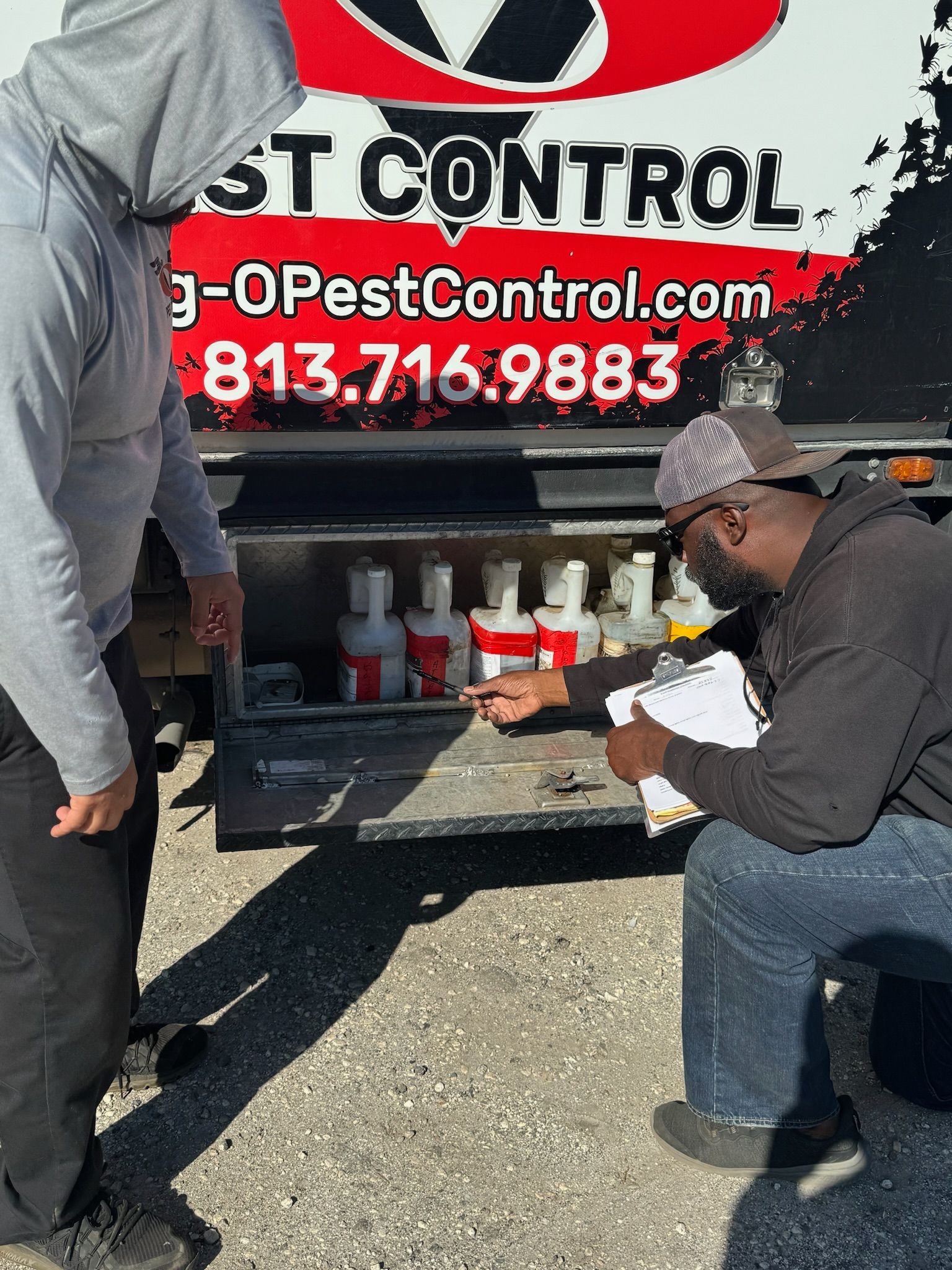 A man is kneeling down in front of a truck that says pest control.