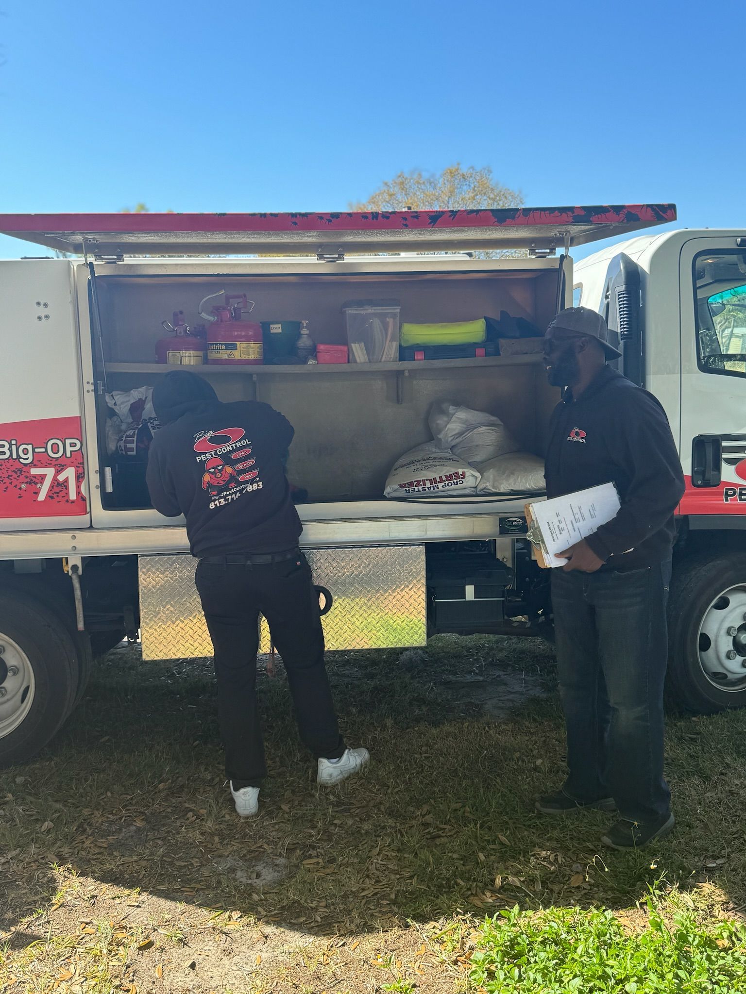 Two men are standing in front of a truck with the back door open.