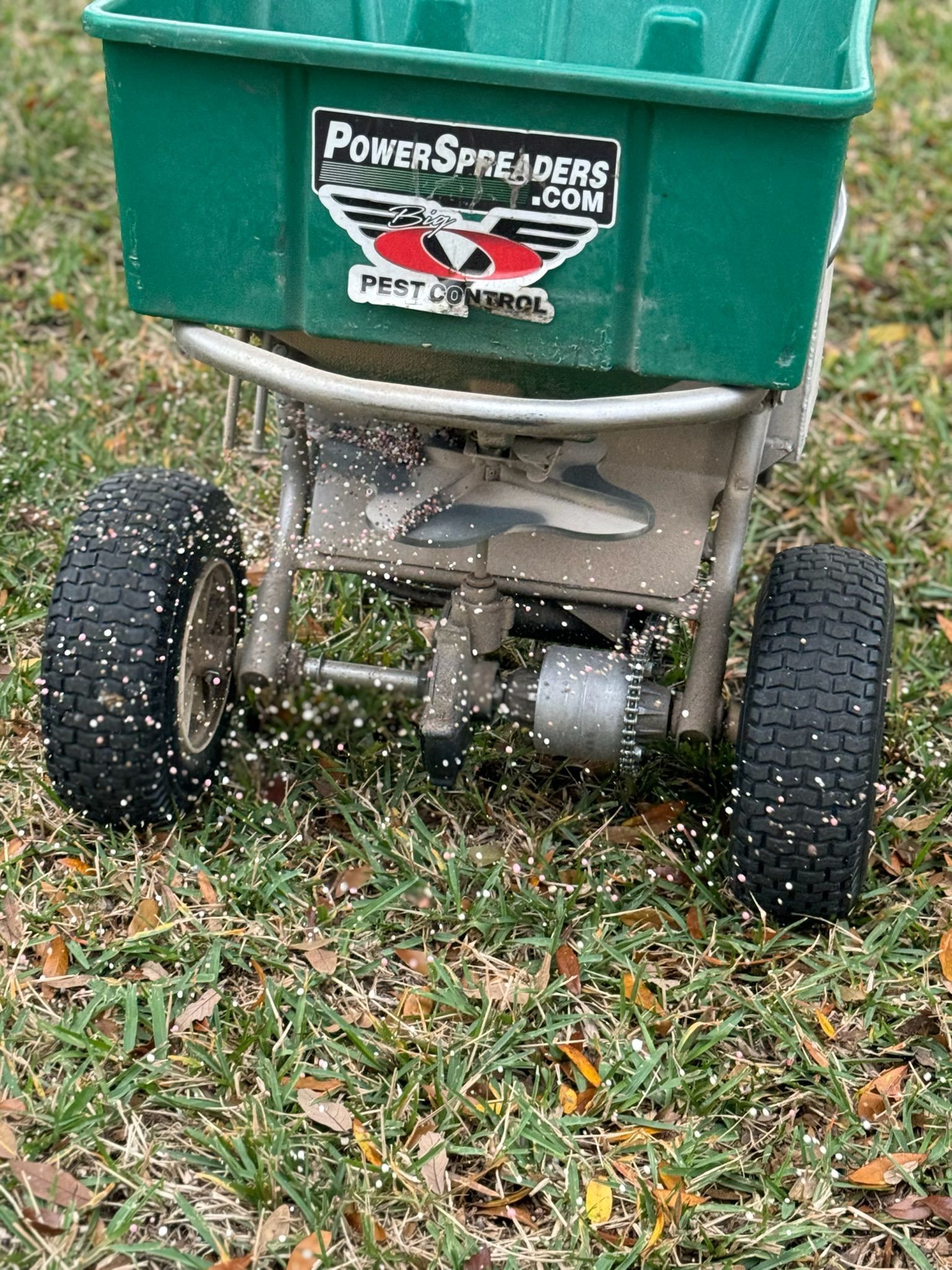 A green spreader is sitting on top of a lush green field.