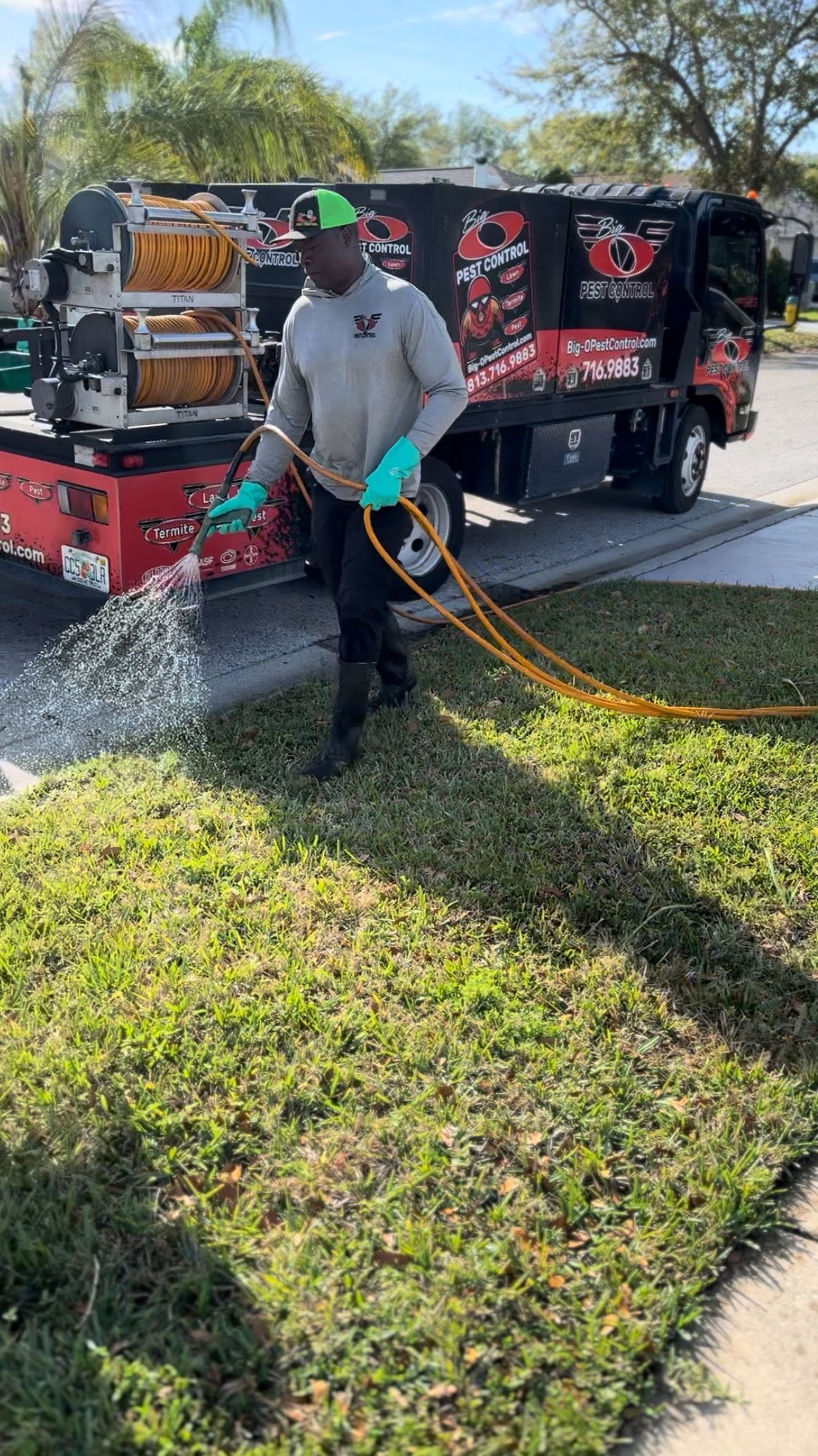 A man is spraying a lawn with a hose in front of a truck.