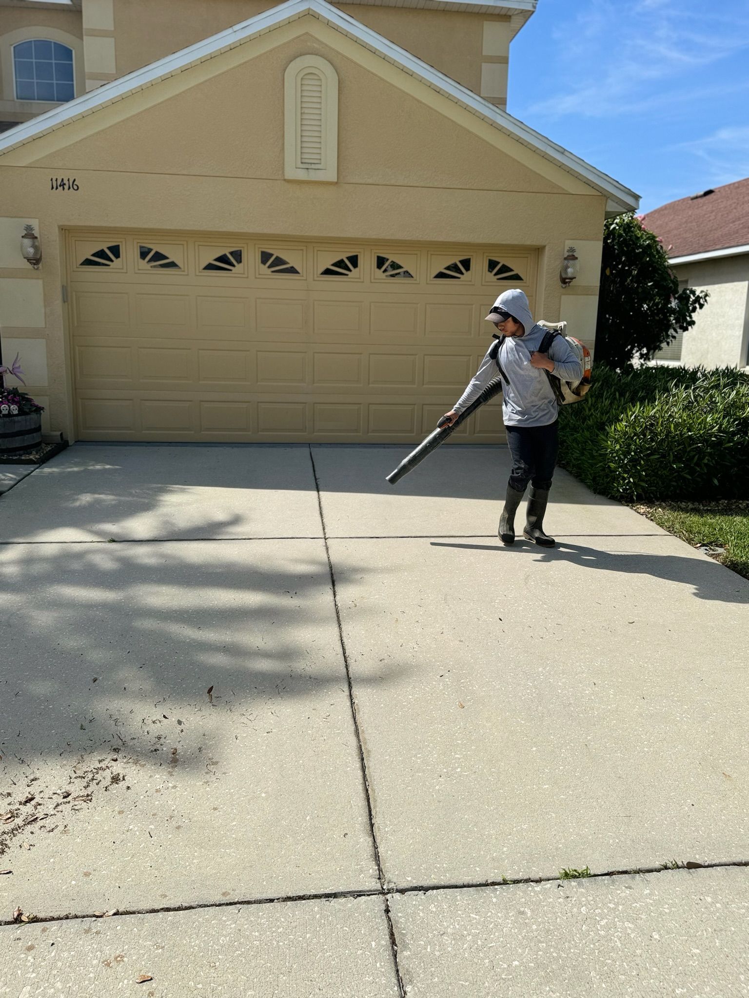 A man is blowing leaves on the sidewalk in front of a house.