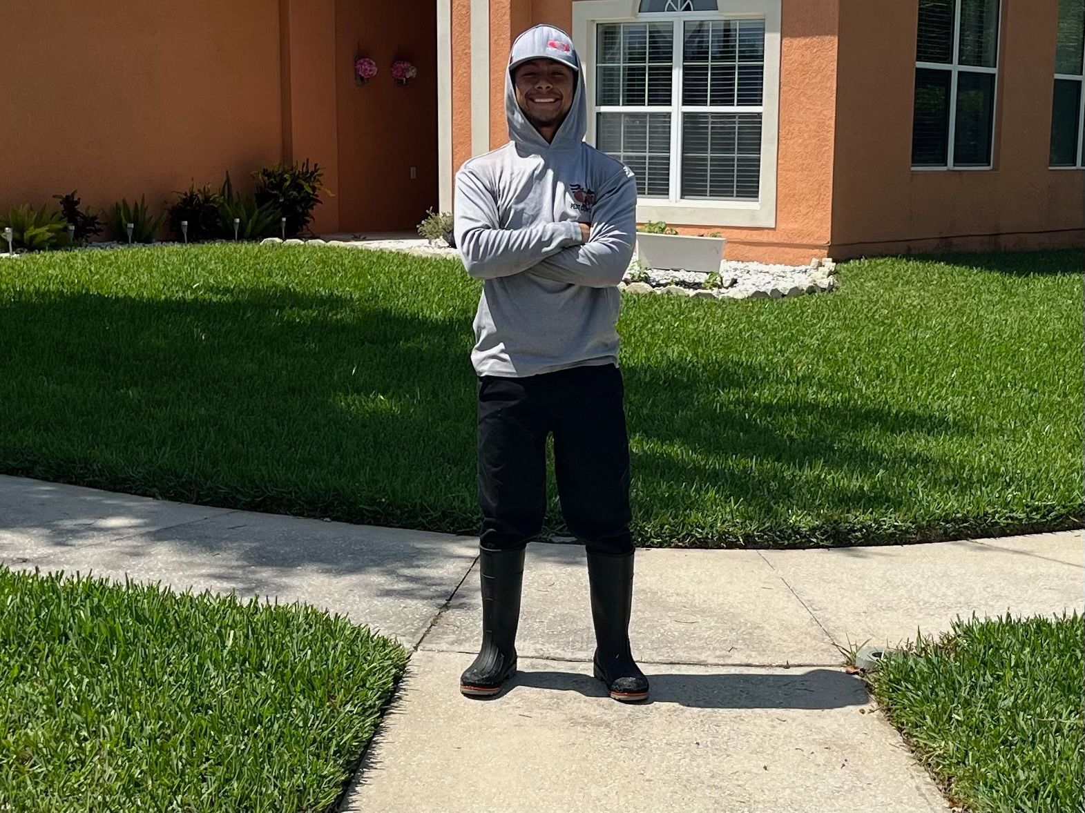 A man is standing on a sidewalk in front of a house with his arms crossed.