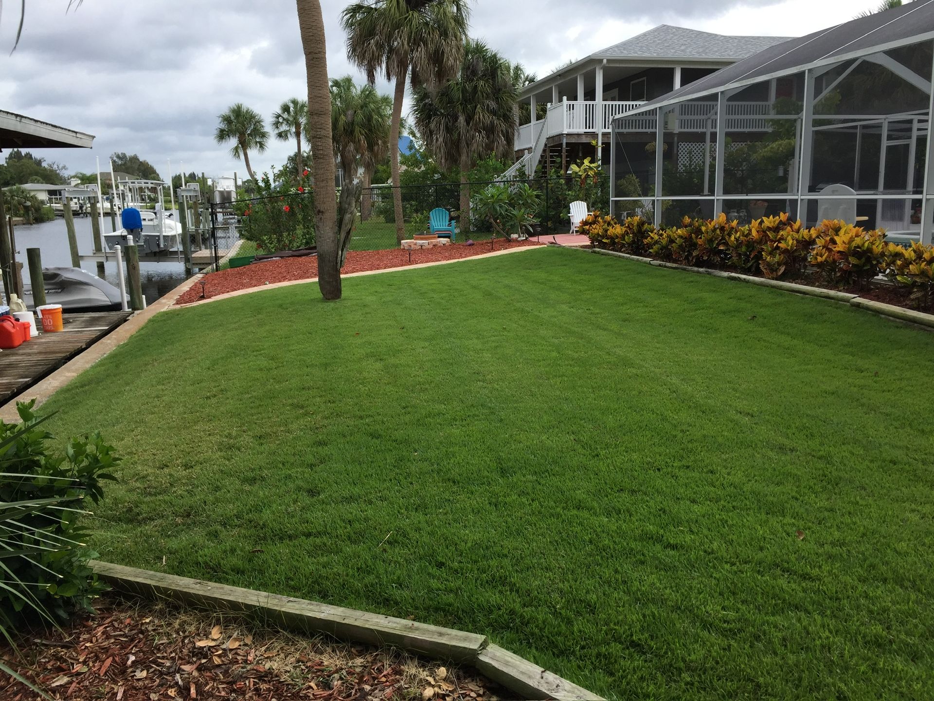 A lush green lawn in front of a house with a dock in the background.