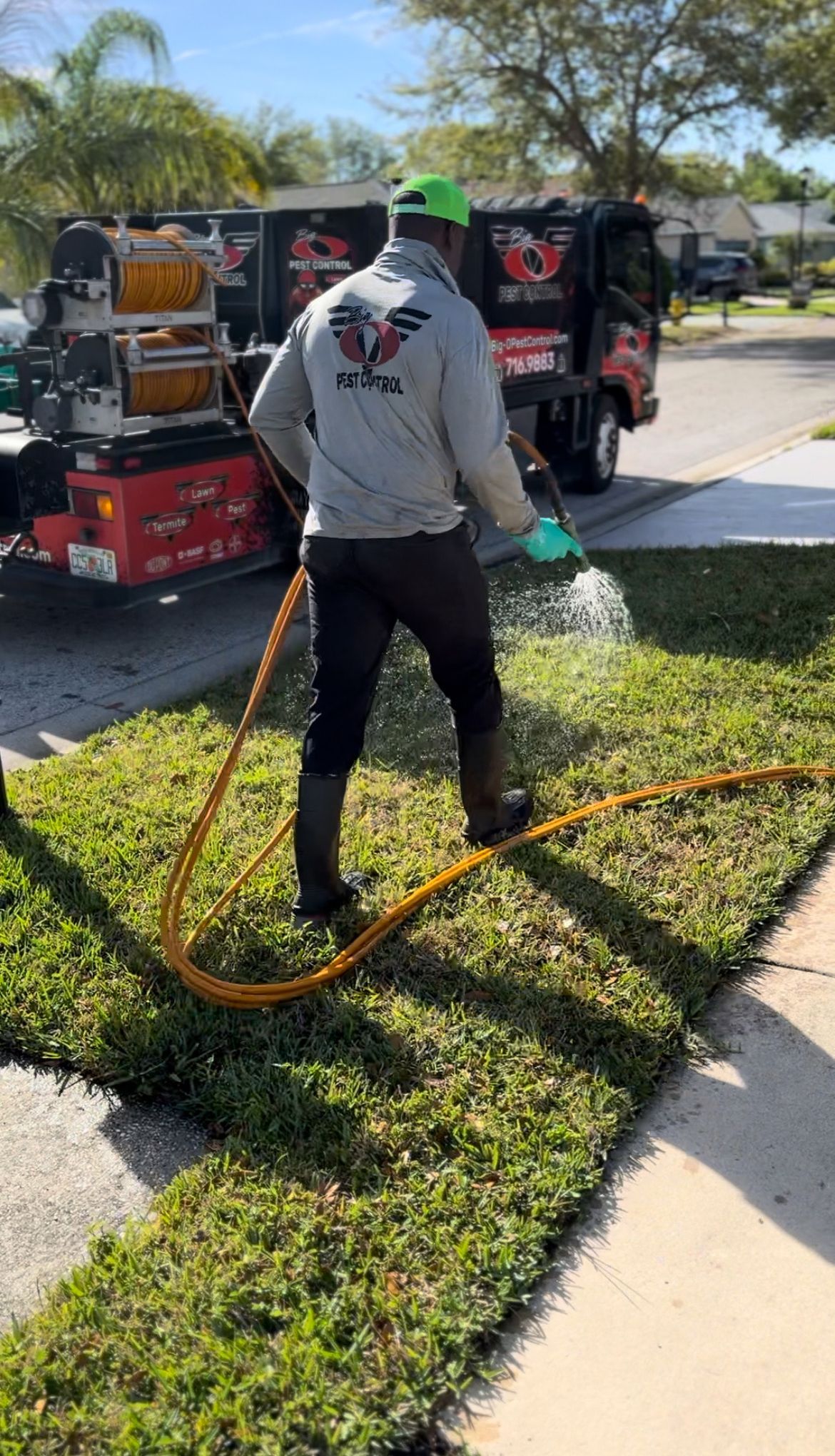 A man is spraying grass with a hose in front of a truck.