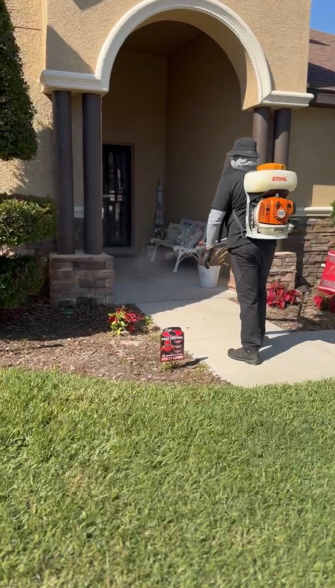 A man is walking in front of a house with a backpack.