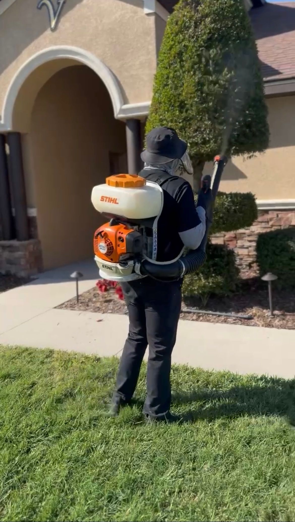 A man is spraying a lawn with a backpack sprayer.
