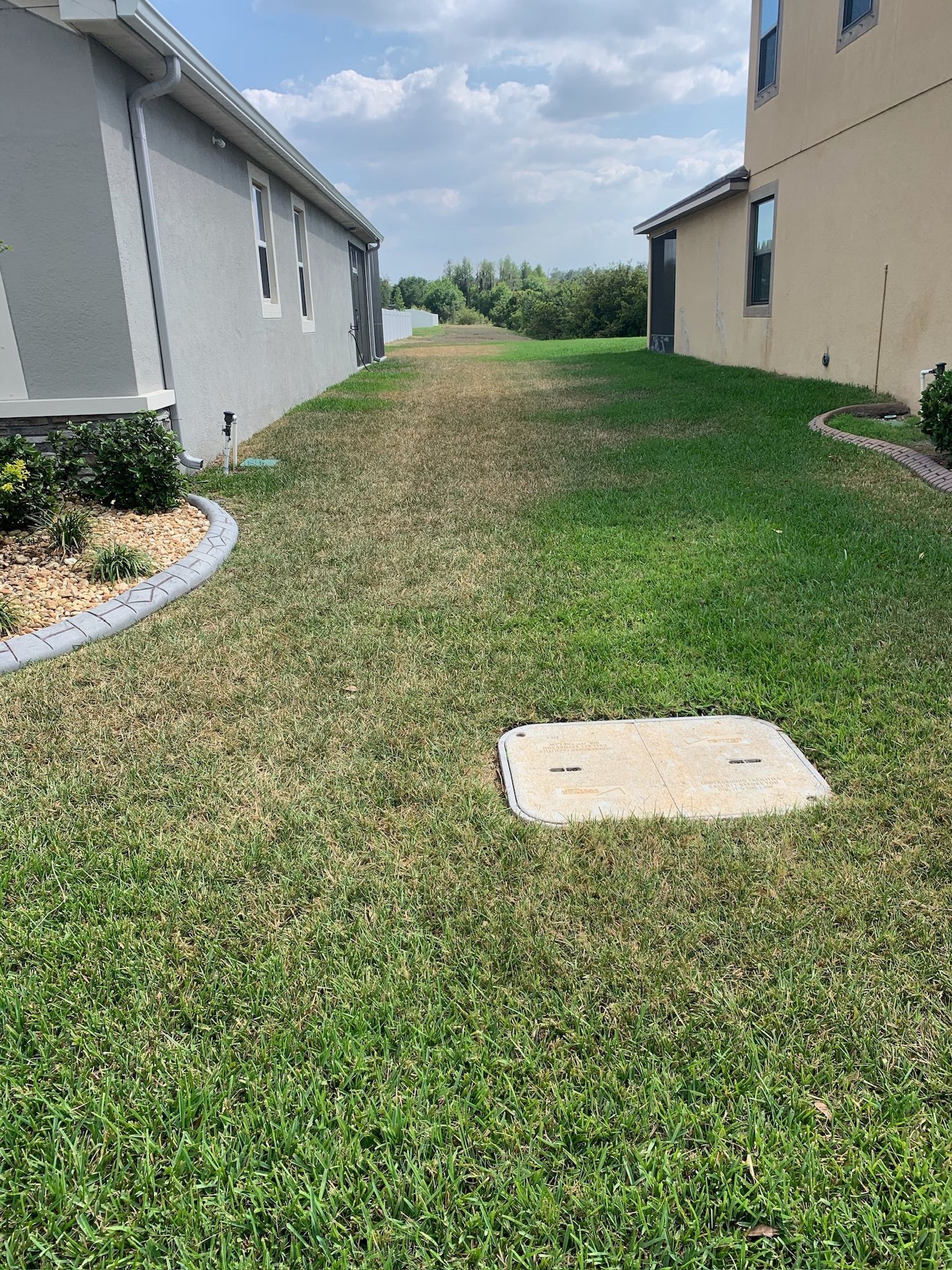 A lawn with a manhole cover in the middle of it next to a house.