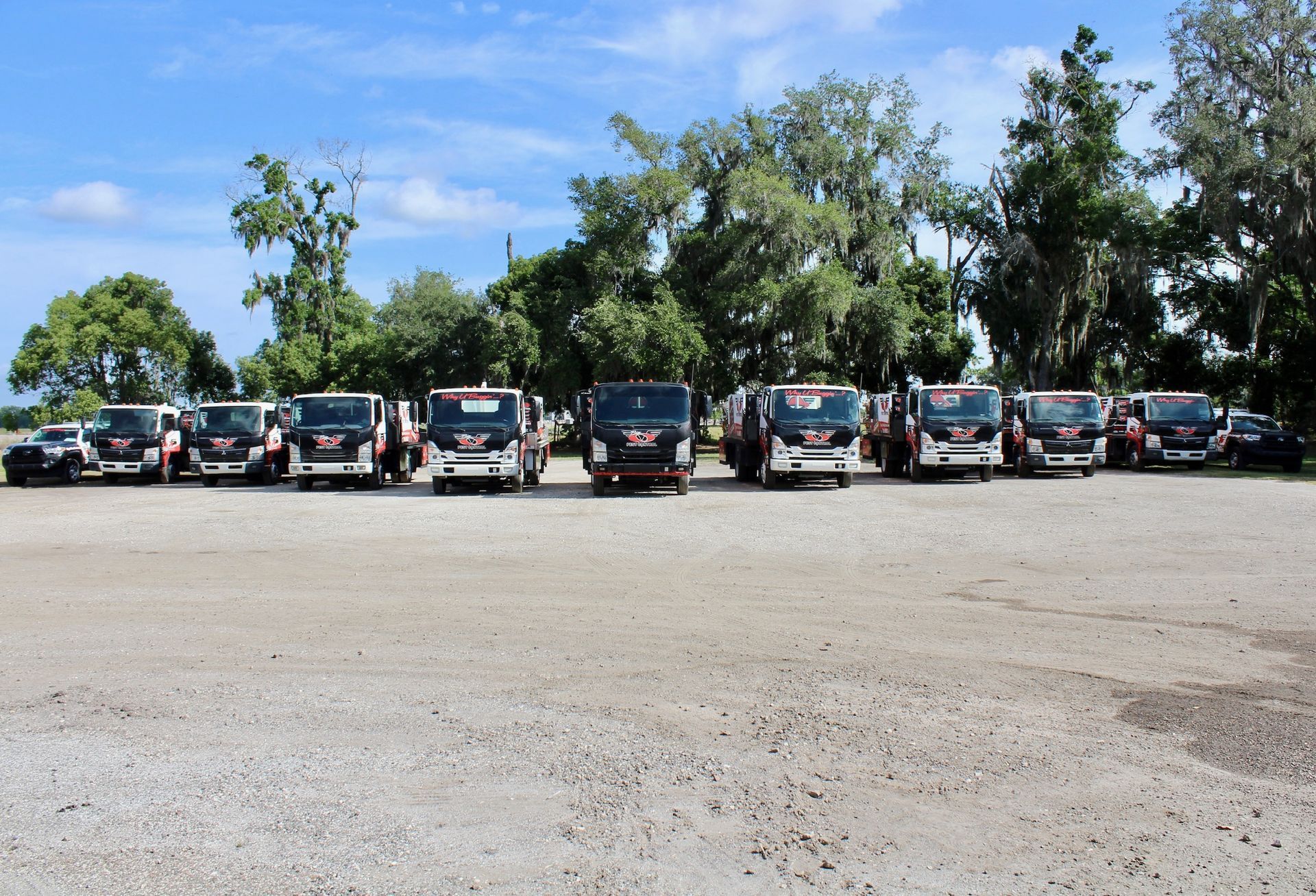 A row of trucks are parked in a gravel lot