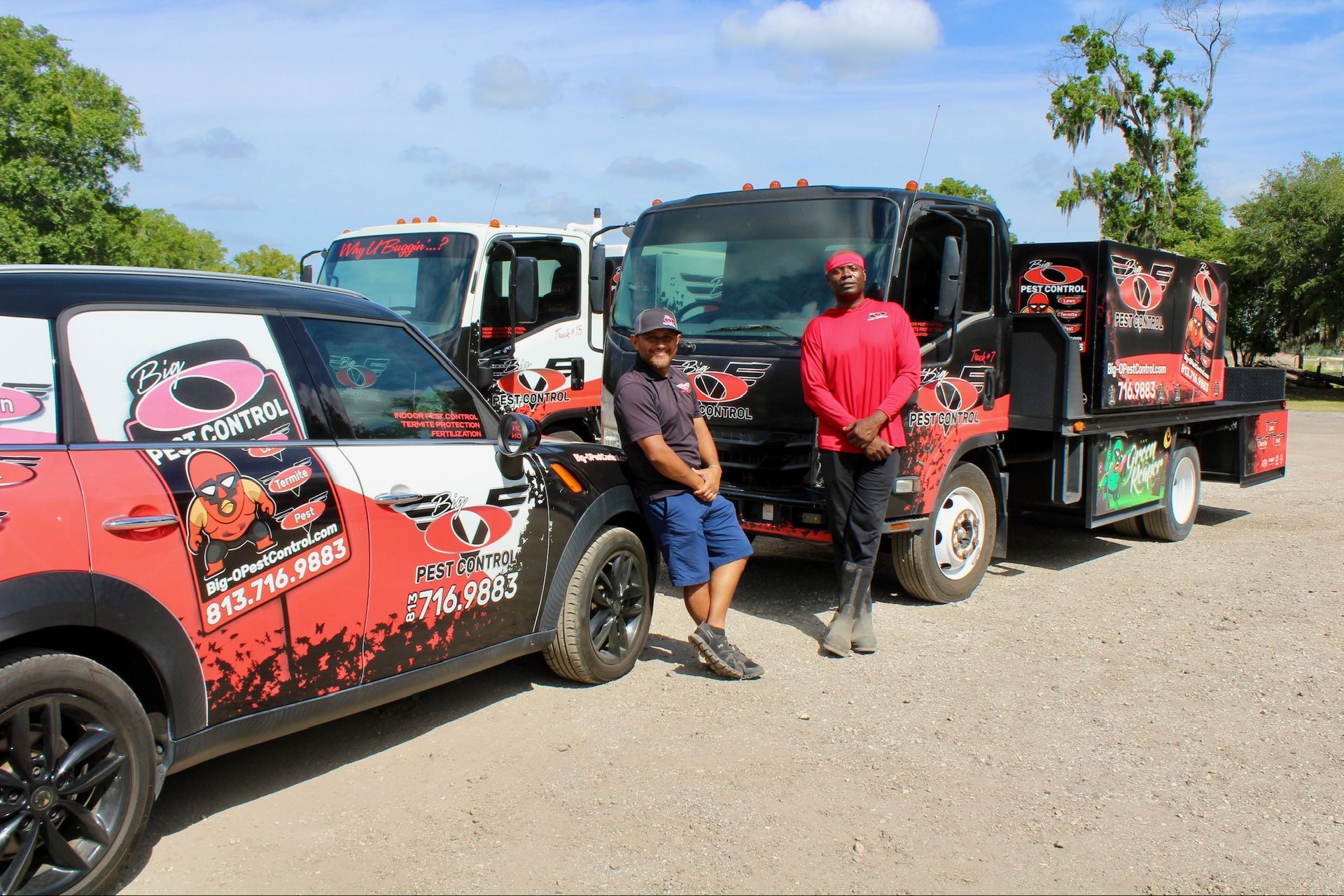 Two men are standing next to a car and a truck in a parking lot.