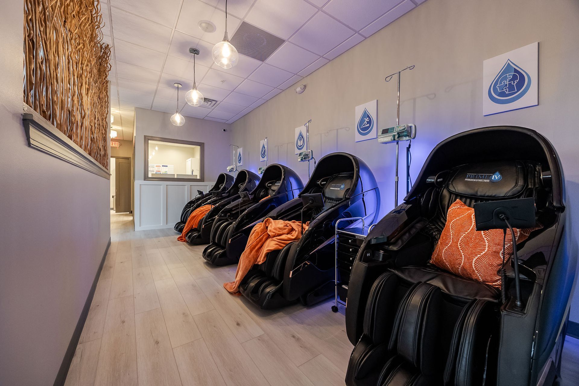 Row of black massage chairs with orange pillows in a softly lit spa lounge.