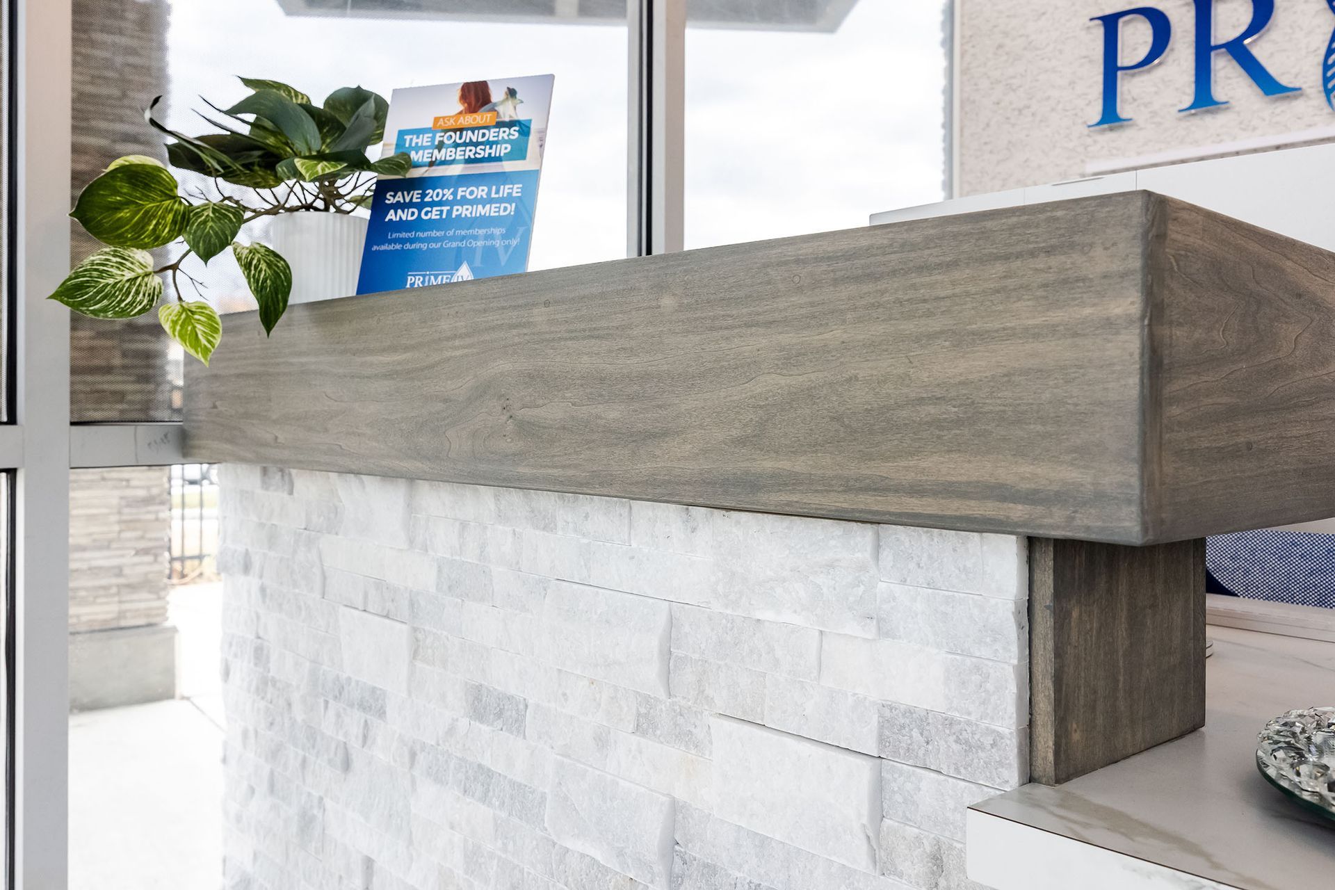 Modern reception desk with a gray wood counter, white stone base, and a small plant by the window.